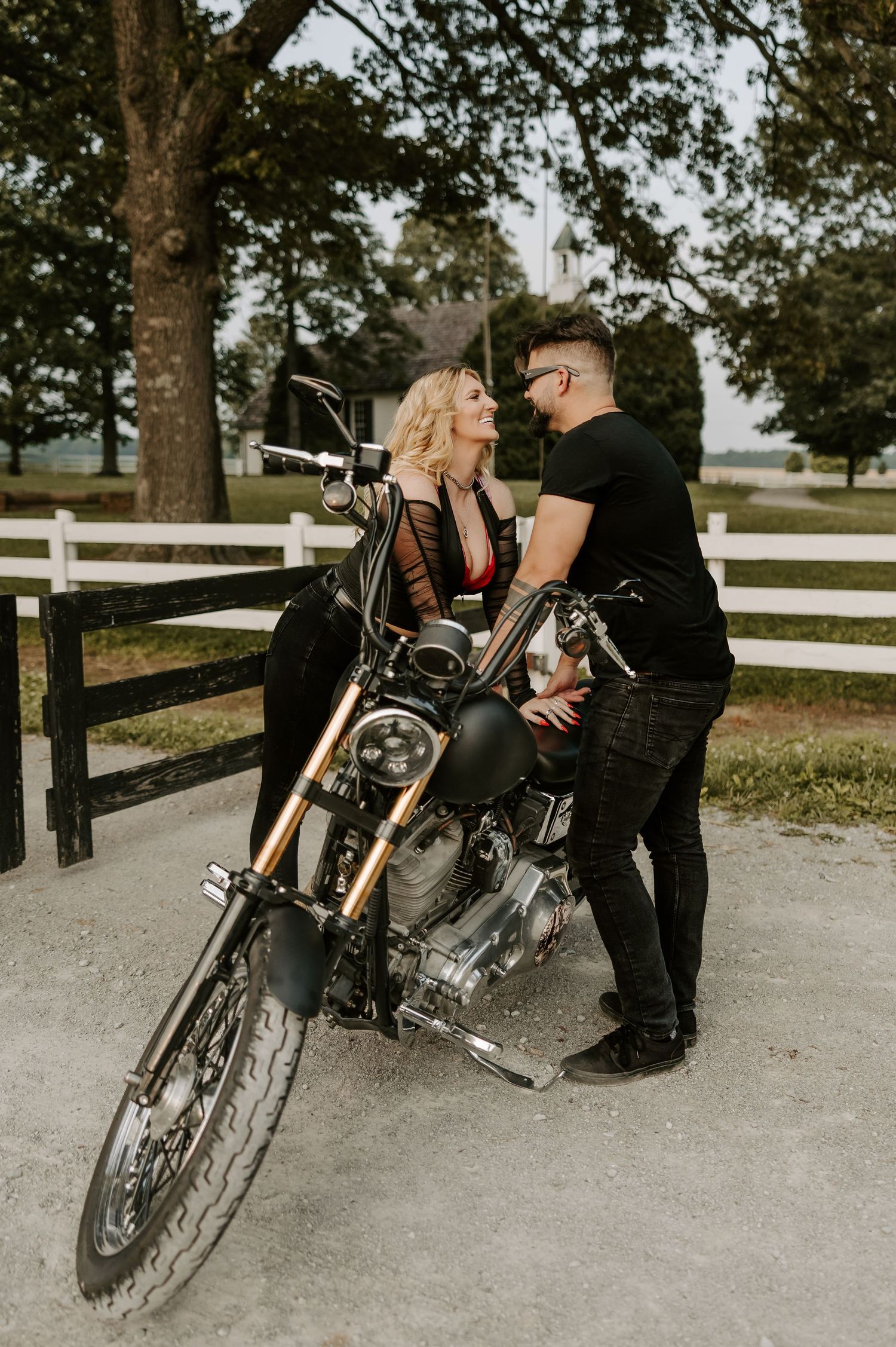 A motorcycle photoshoot scene with a black custom bike against a rustic farm backdrop.