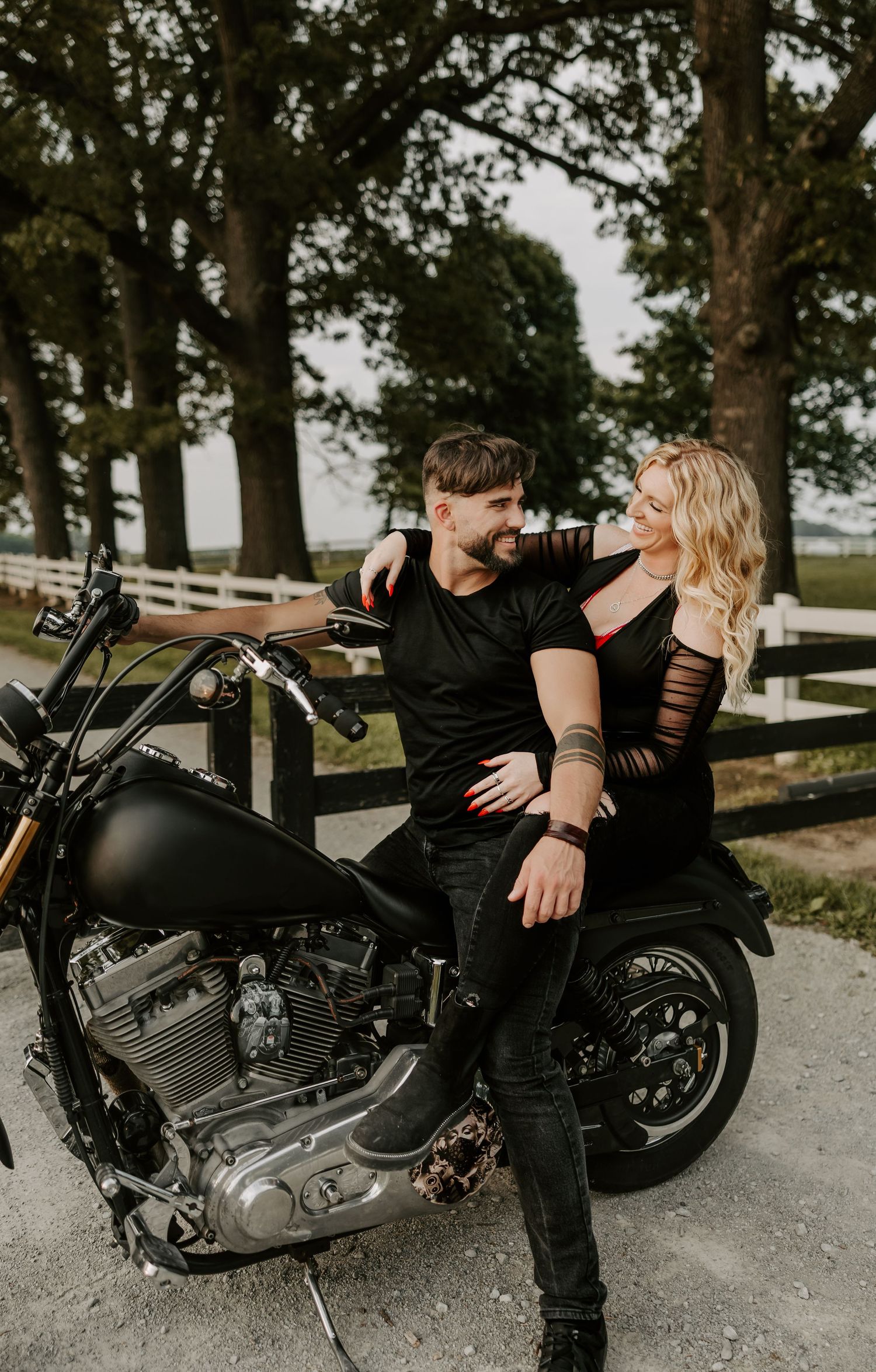 Stylish couple shares intimate moment while sitting on parked motorcycle outdoors.