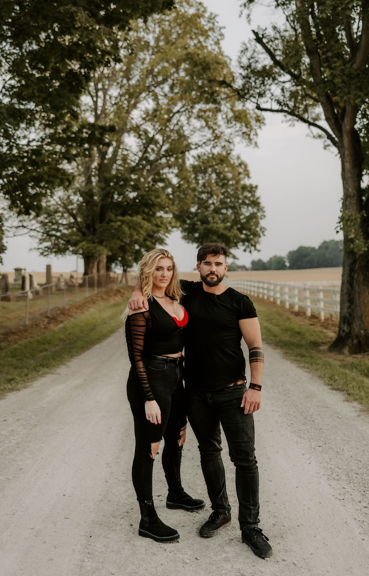 Couple in matching black outfits poses together on rural gravel road.