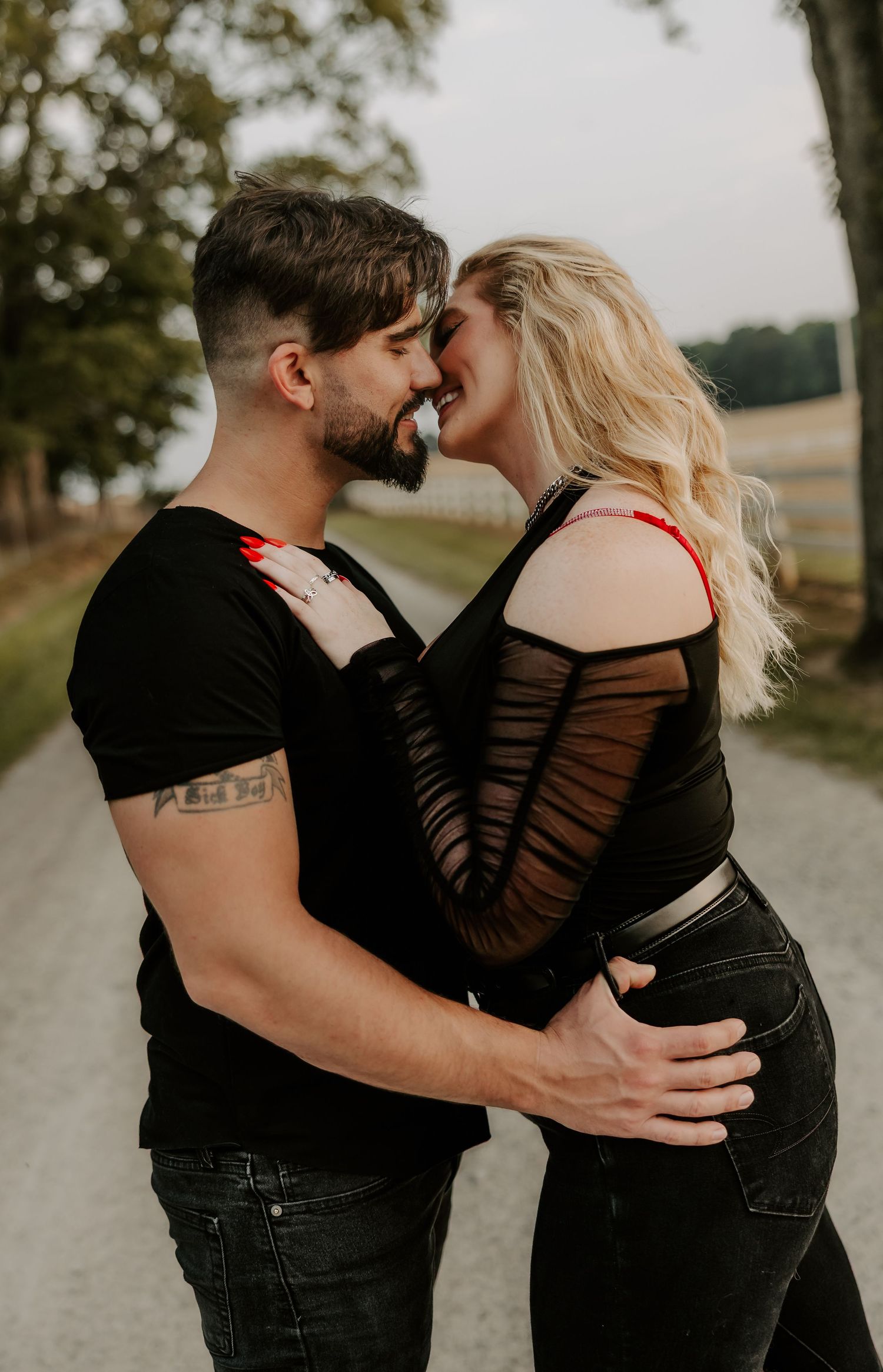 Romantic couple in black clothing embraces near motorcycle on country path.