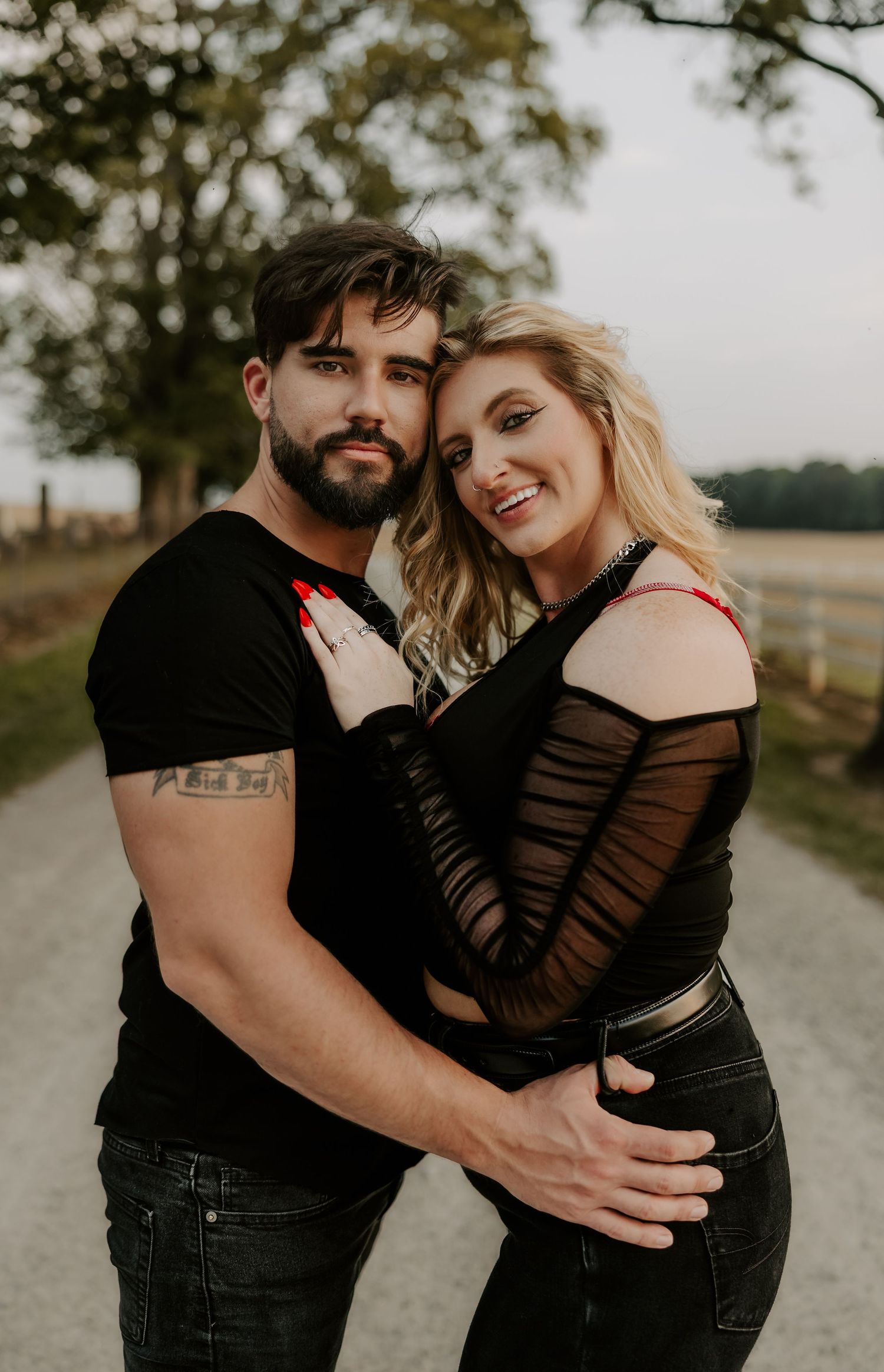 Couple shares tender moment together on rural path with trees in background.