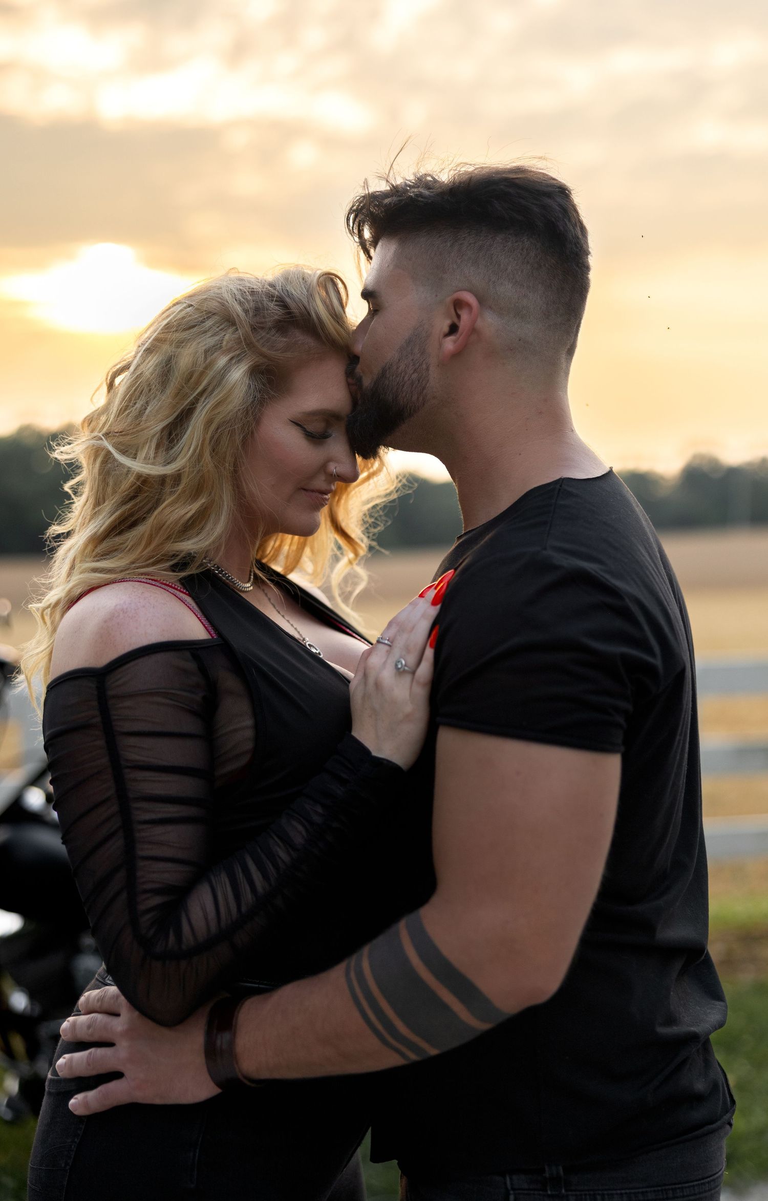 A tender moment between a couple at golden hour with a motorcycle in the background.