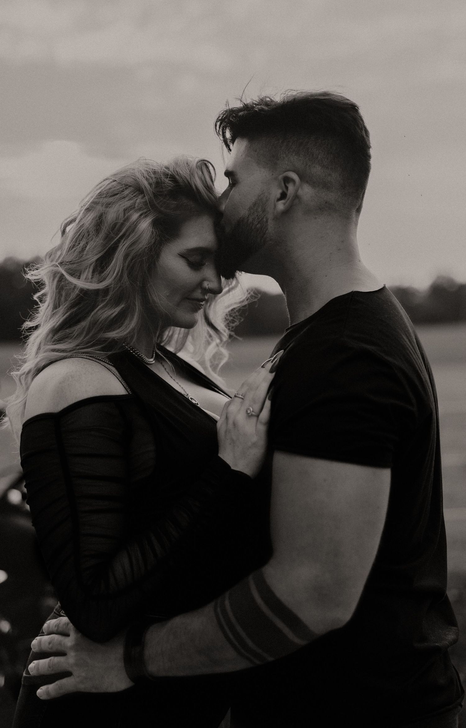 An intimate black and white portrait of a couple embracing outdoors.