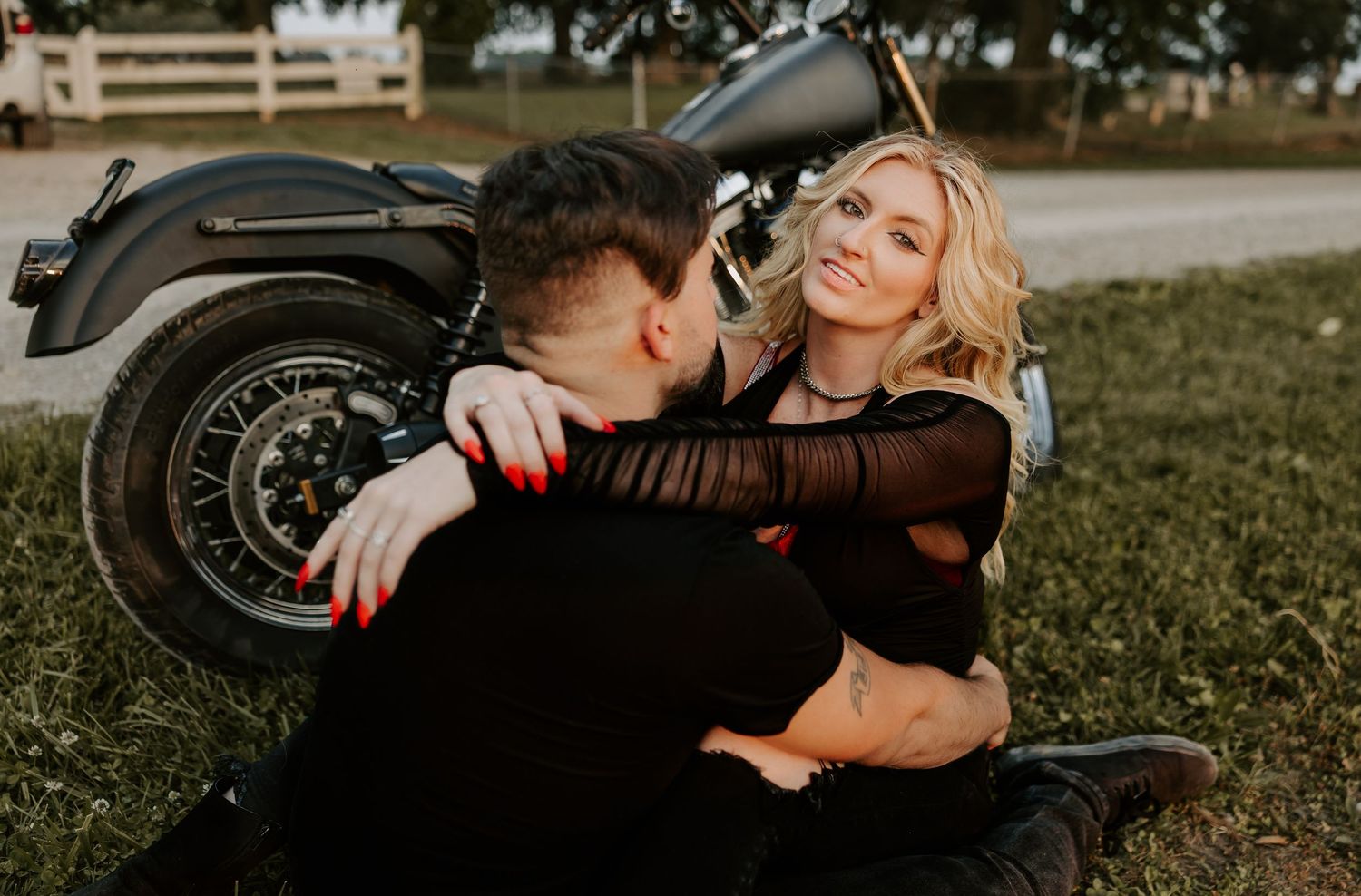 A couple embracing beside a motorcycle on grass during a romantic photoshoot.