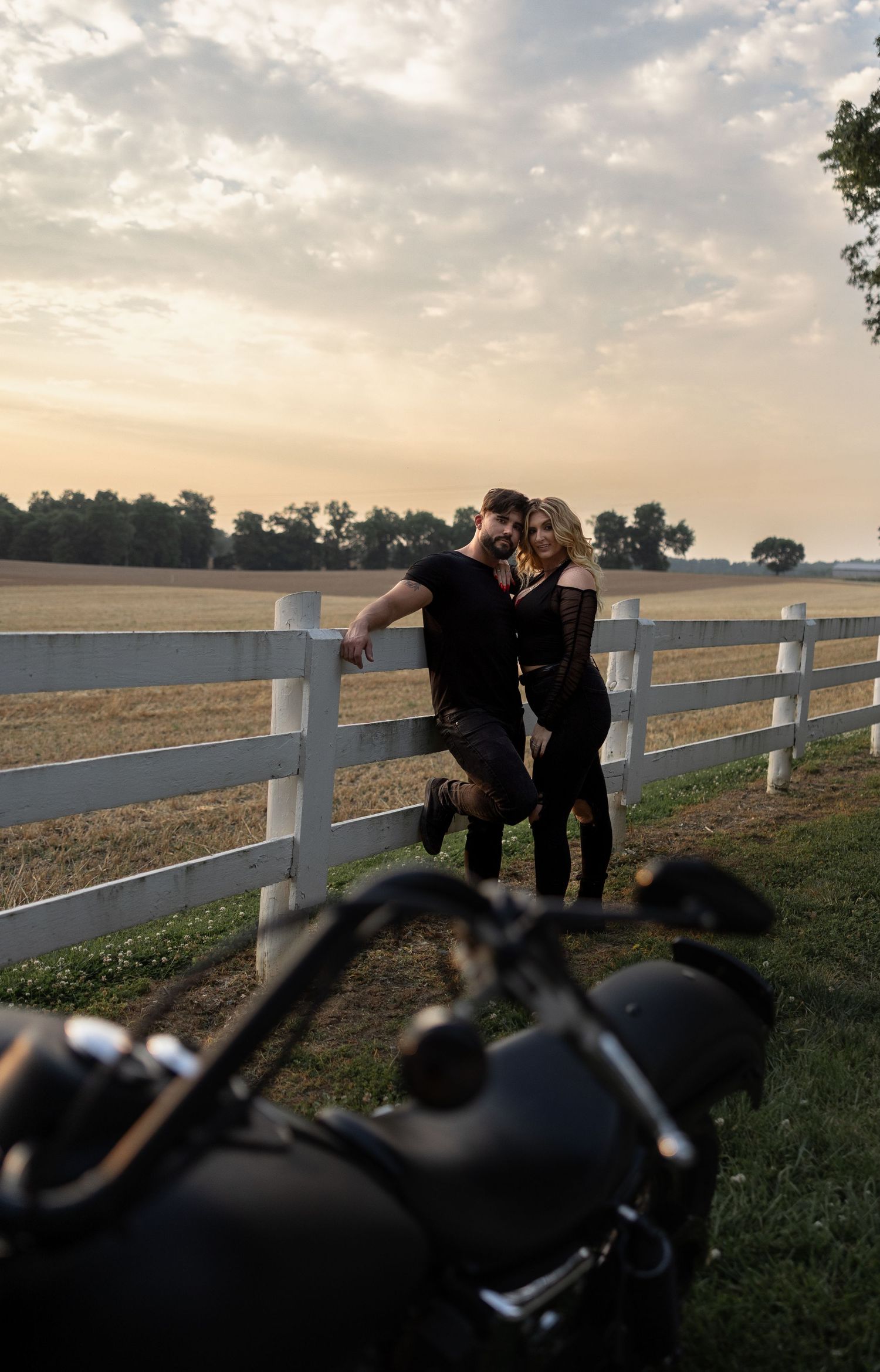 A couple dancing together at sunset with a motorcycle and white fence in view.