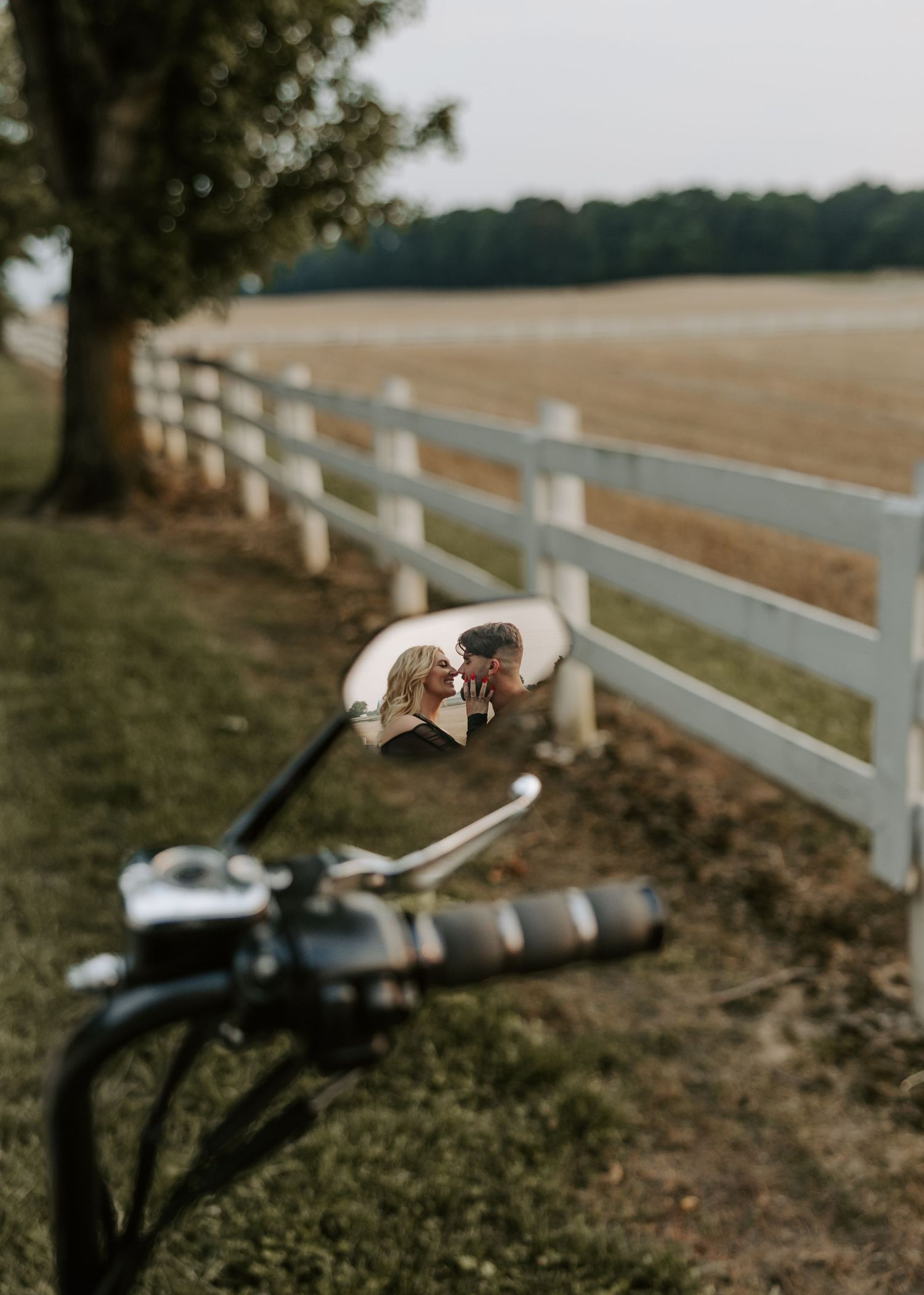A creative motorcycle mirror reflection shot capturing a couple by a white fence.