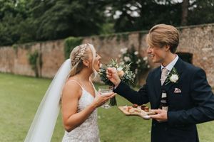 A bride and groom share a joyful moment together while enjoying wedding cake in an outdoor garden setting.
