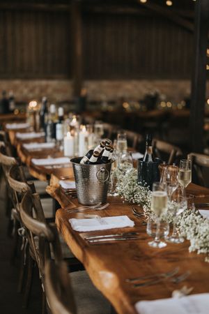 Rustic wedding reception table set with wine bottles, baby's breath flowers and candles on wooden farmhouse tables.