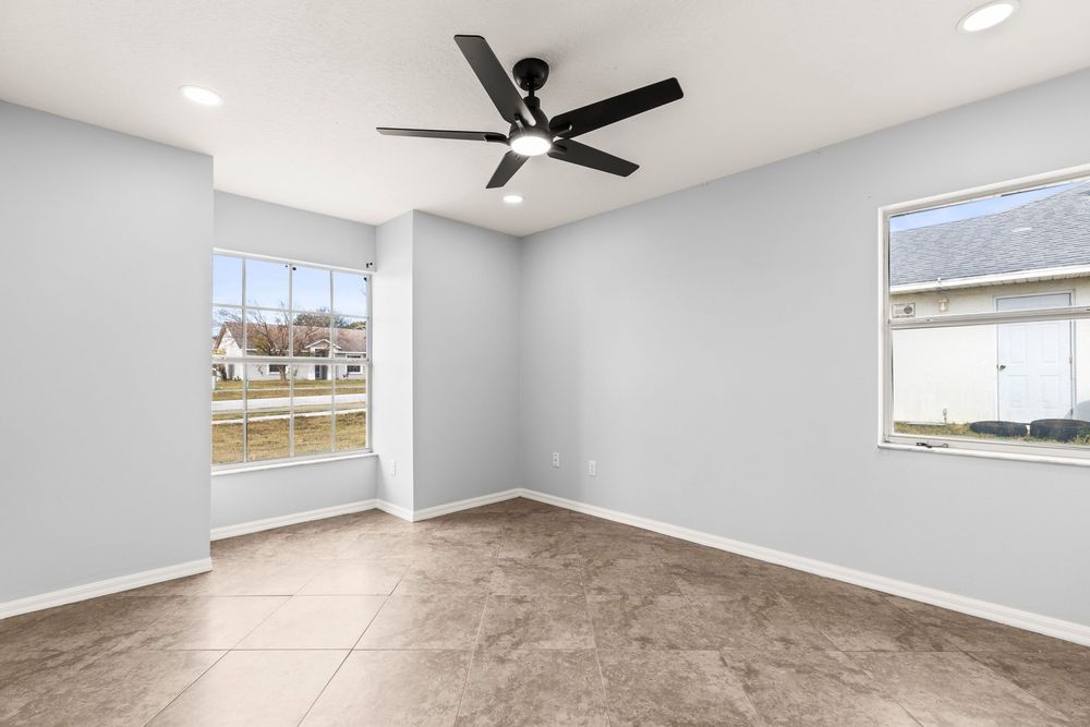 Empty room with gray walls, ceiling fan, and two windows offering natural light.