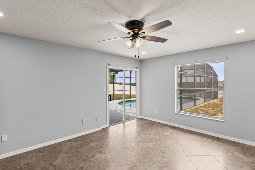 Bright empty bedroom with large windows, ceiling fan, and gray walls.
