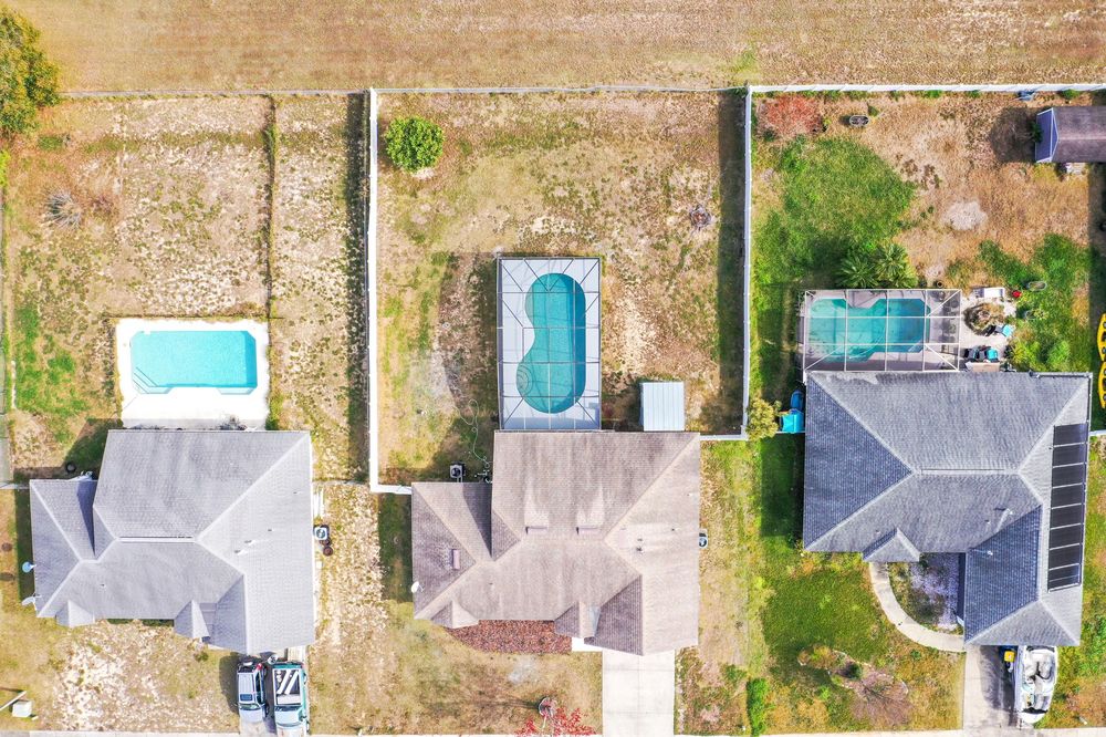 Aerial view of three suburban houses with swimming pools and backyards arranged in a row.