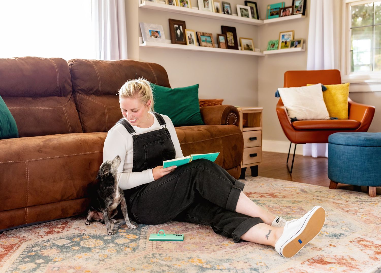 Person lying on patterned rug reading book in cozy living room with brown couch.