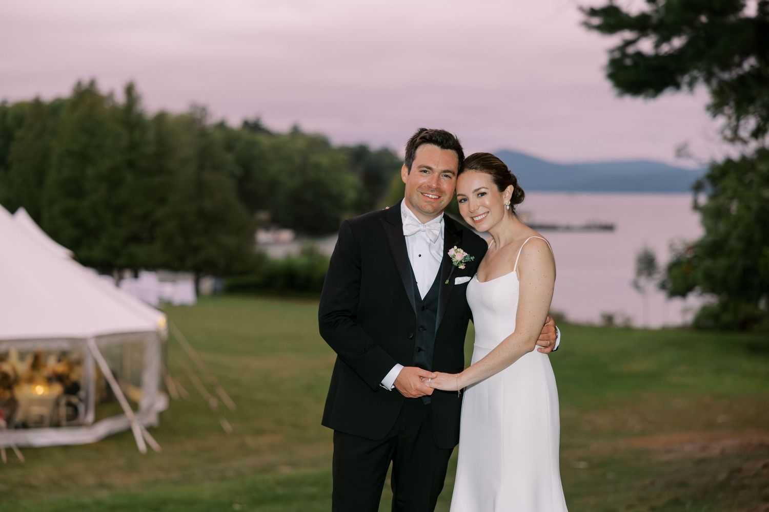 A couple shares romantic moments during a lakeside wedding celebration as the sun sets over scenic mountain views.