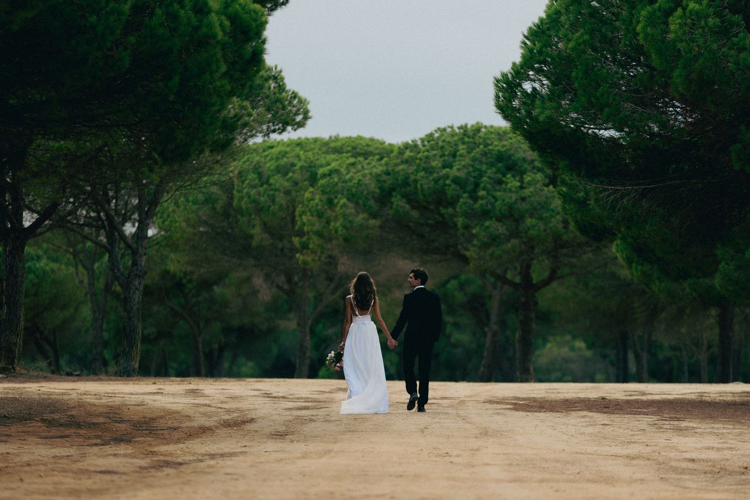 Bride in flowing white dress walking along misty beach leaving footprints in sand during wedding.