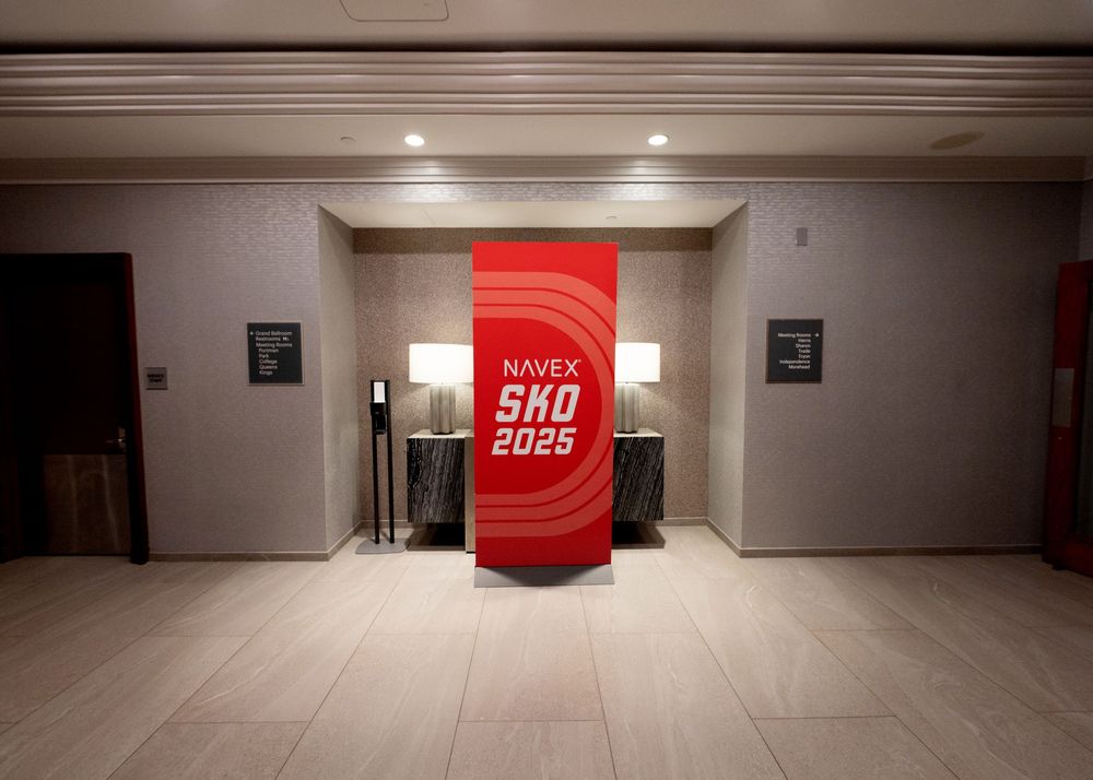 Minimalist hallway with red SHO 2025 branded display between elevator doors.