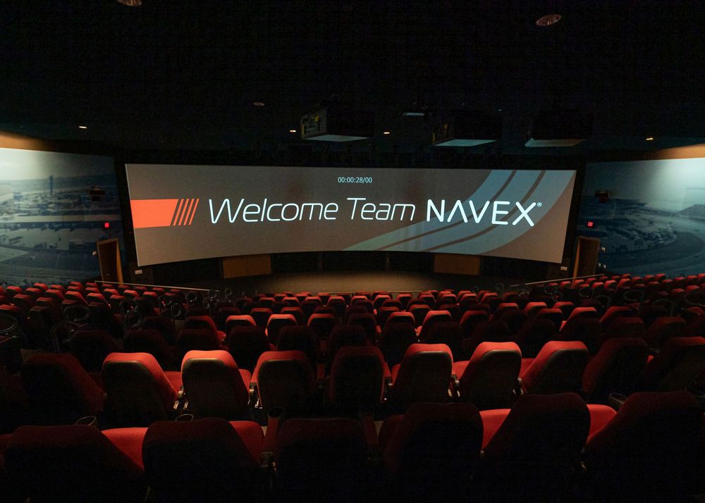 Theater auditorium with Welcome Team NAVEX displayed on the presentation screen.