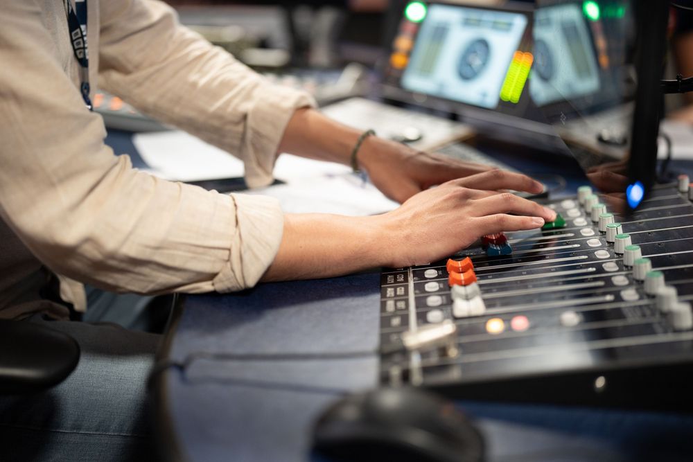 Audio engineer operates a professional mixing console with faders and knobs in a recording studio environment.