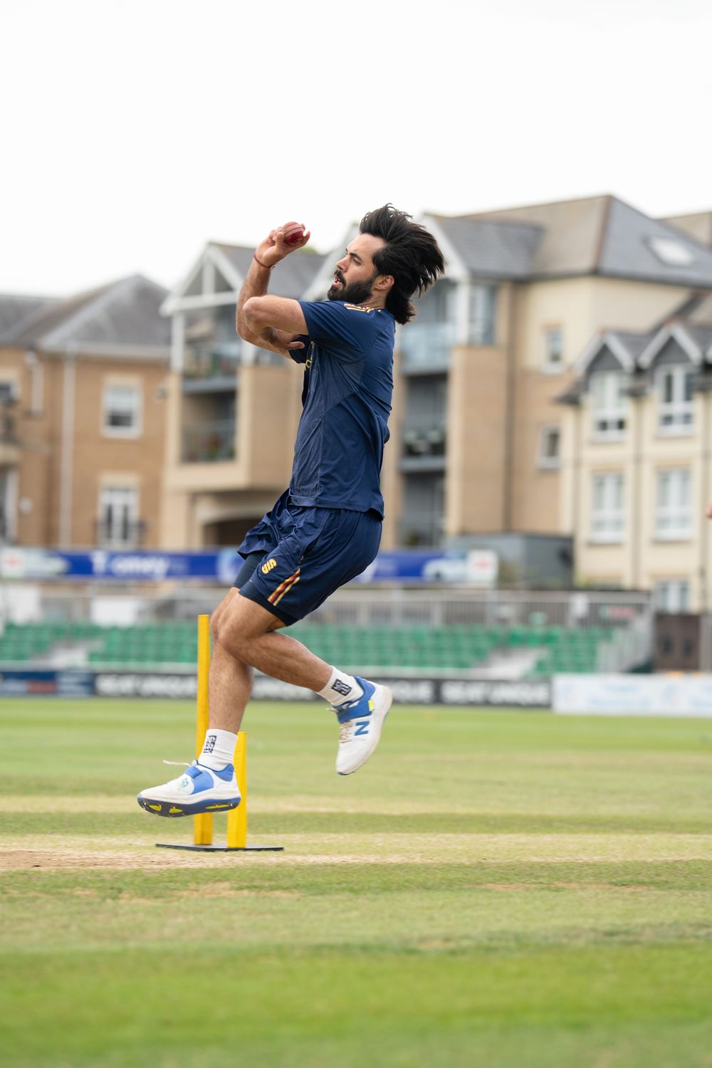 A sequence of cricket bowling action shots shows a player's delivery stride and follow through on a grass field near houses.
