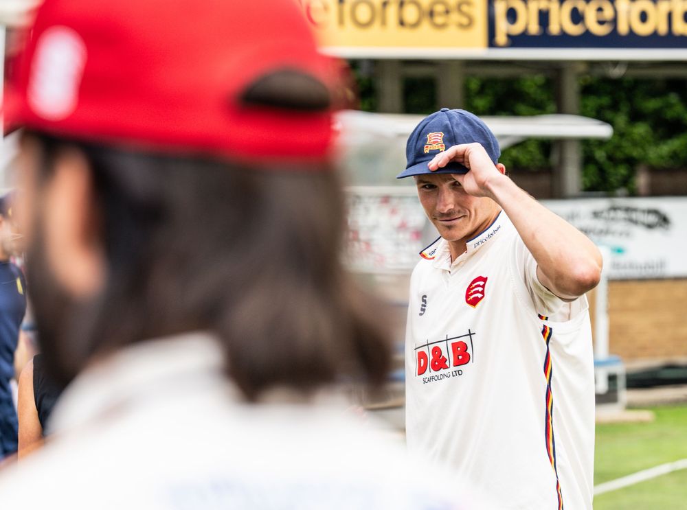 Baseball player in red cap and white uniform adjusts his hat while having a conversation on the field.
