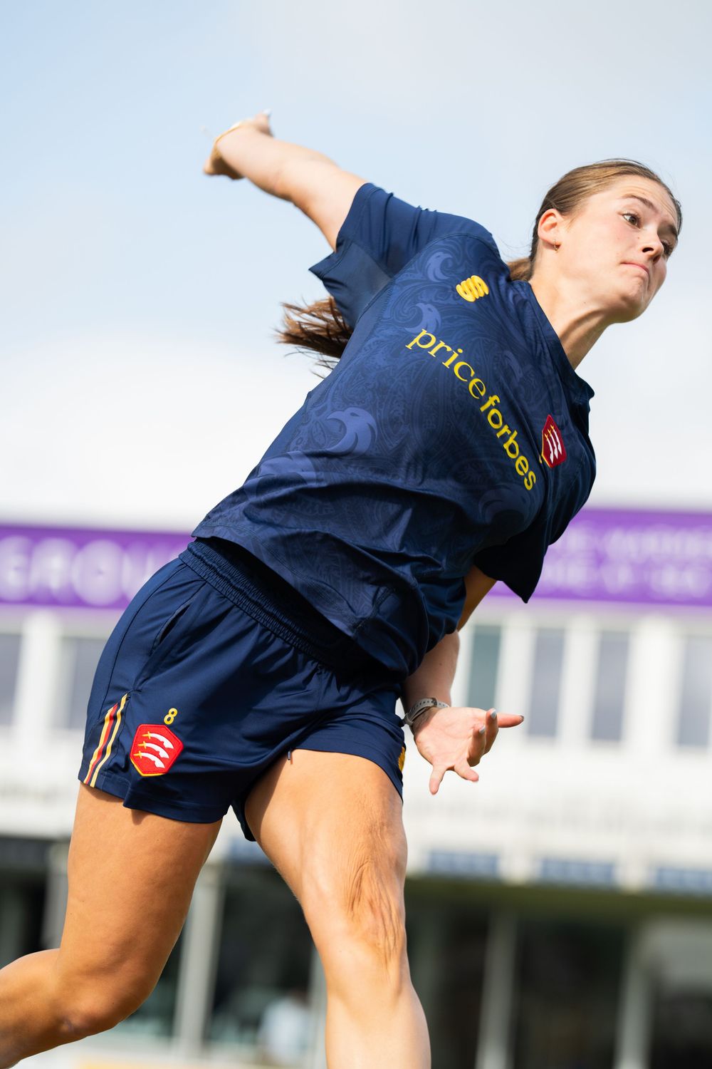 Cricket player in navy blue uniform performs a bowling action during a match.