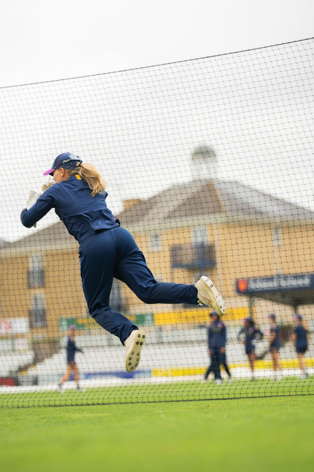 Soccer goalkeeper wearing navy uniform makes a dramatic diving save in front of goal net during practice session.