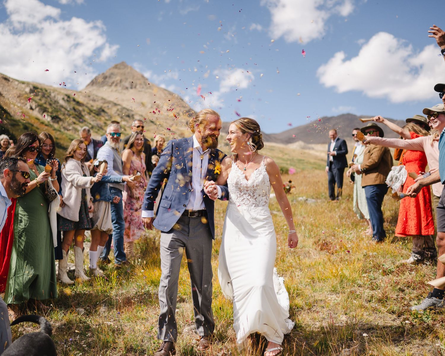 Wedding guests throwing flower petals in celebration against a mountain backdrop.