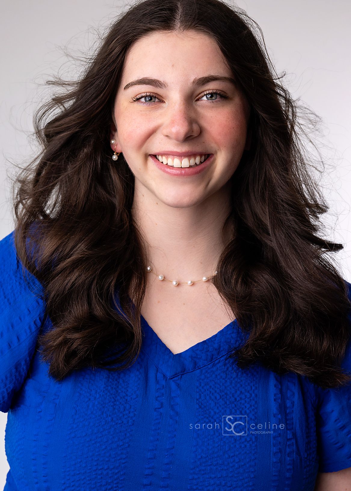Woman in bright blue sweater smiling with flowing dark hair in dynamic motion poses against white background.