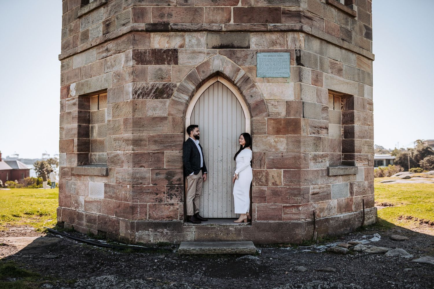 Two people stand in opposite doorways of an old stone church tower with Gothic arched entrances.