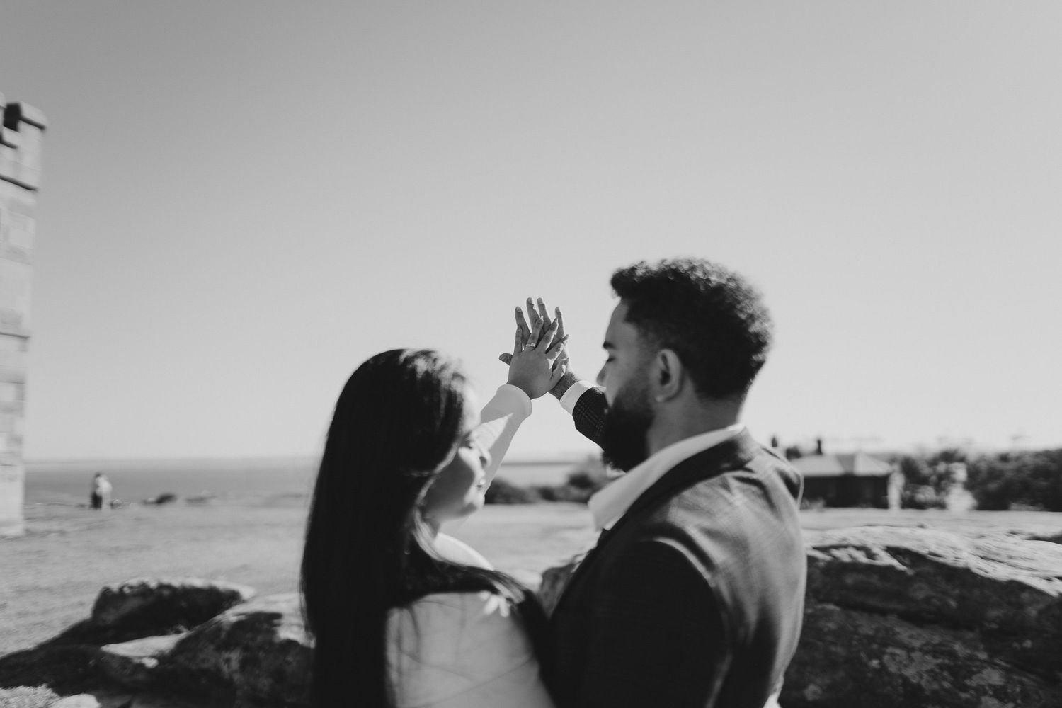 A romantic black and white photograph of a couple sharing a tender moment on rocky coastal cliffs.