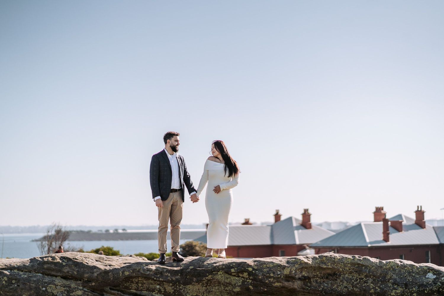 Couple sharing tender moment by the ocean on a bright sunny day with sparkles on the water.