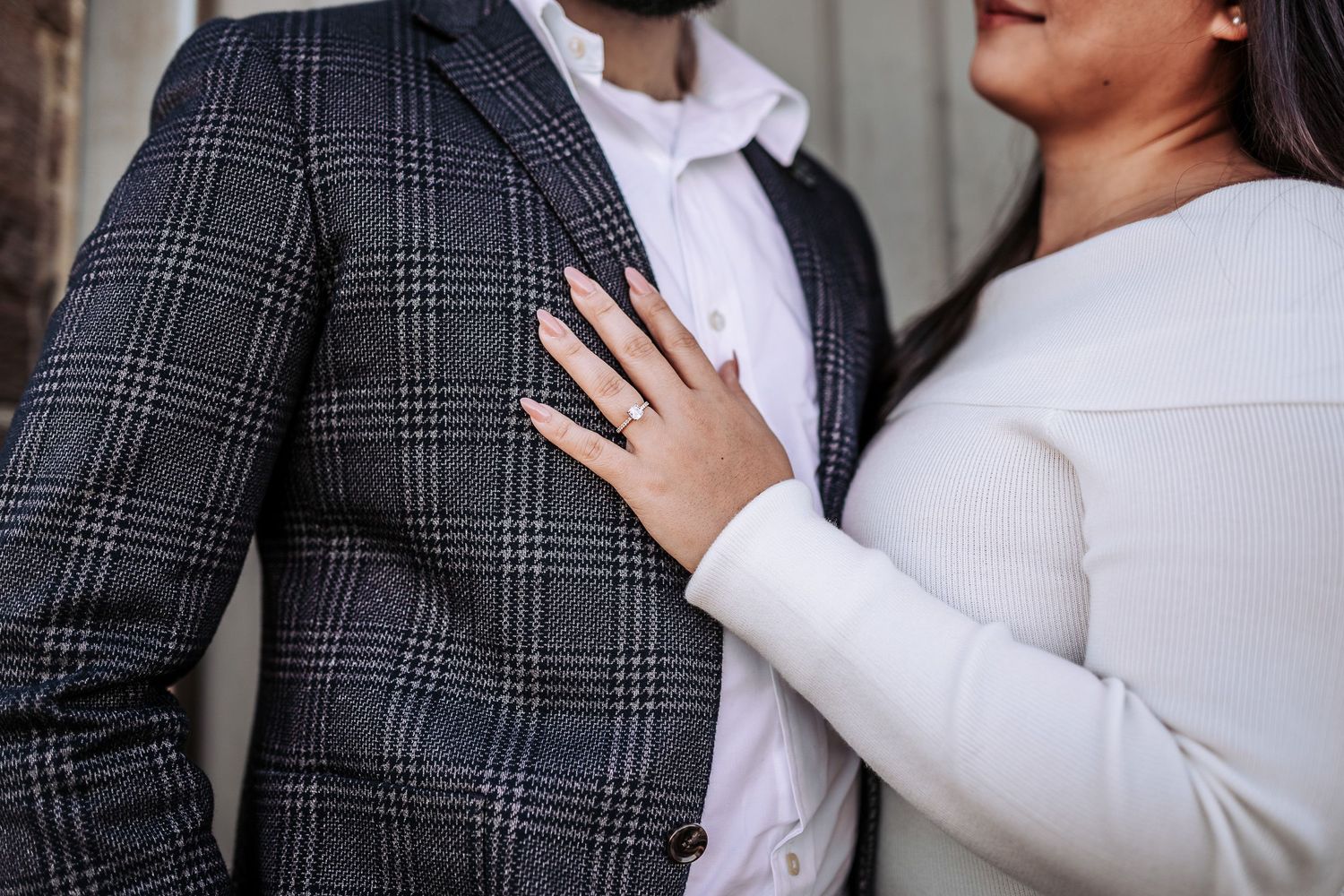 Close up of couple during engagement photo shoot showing plaid suit jacket and white clothing details.
