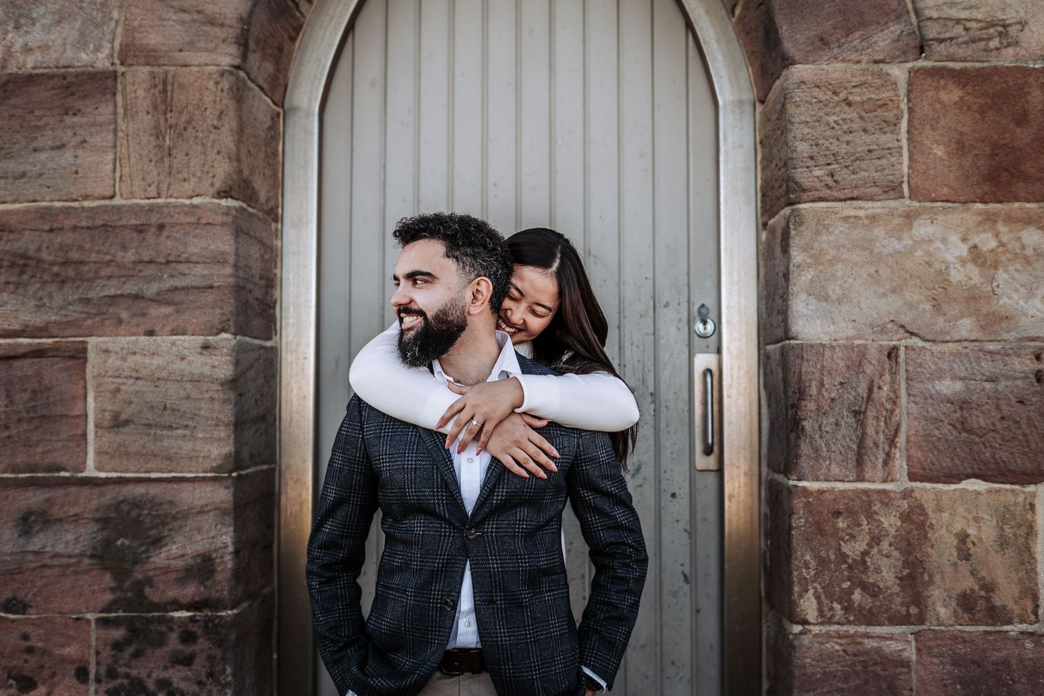 A series of intimate moments captured against a rustic stone wall with wooden doors in black and white tones.