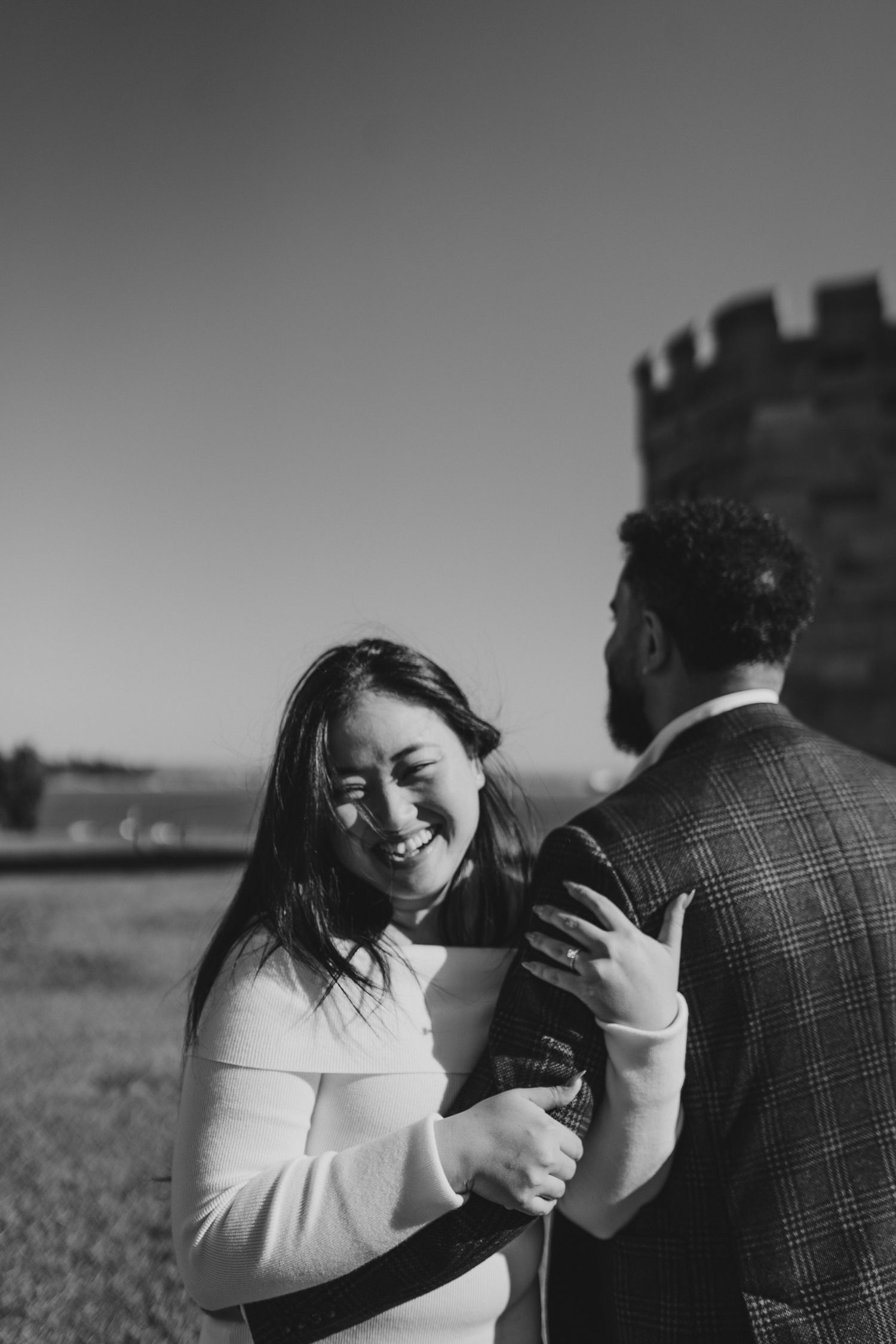 Couple shares joyful moment together in black and white photo with castle silhouette in background.