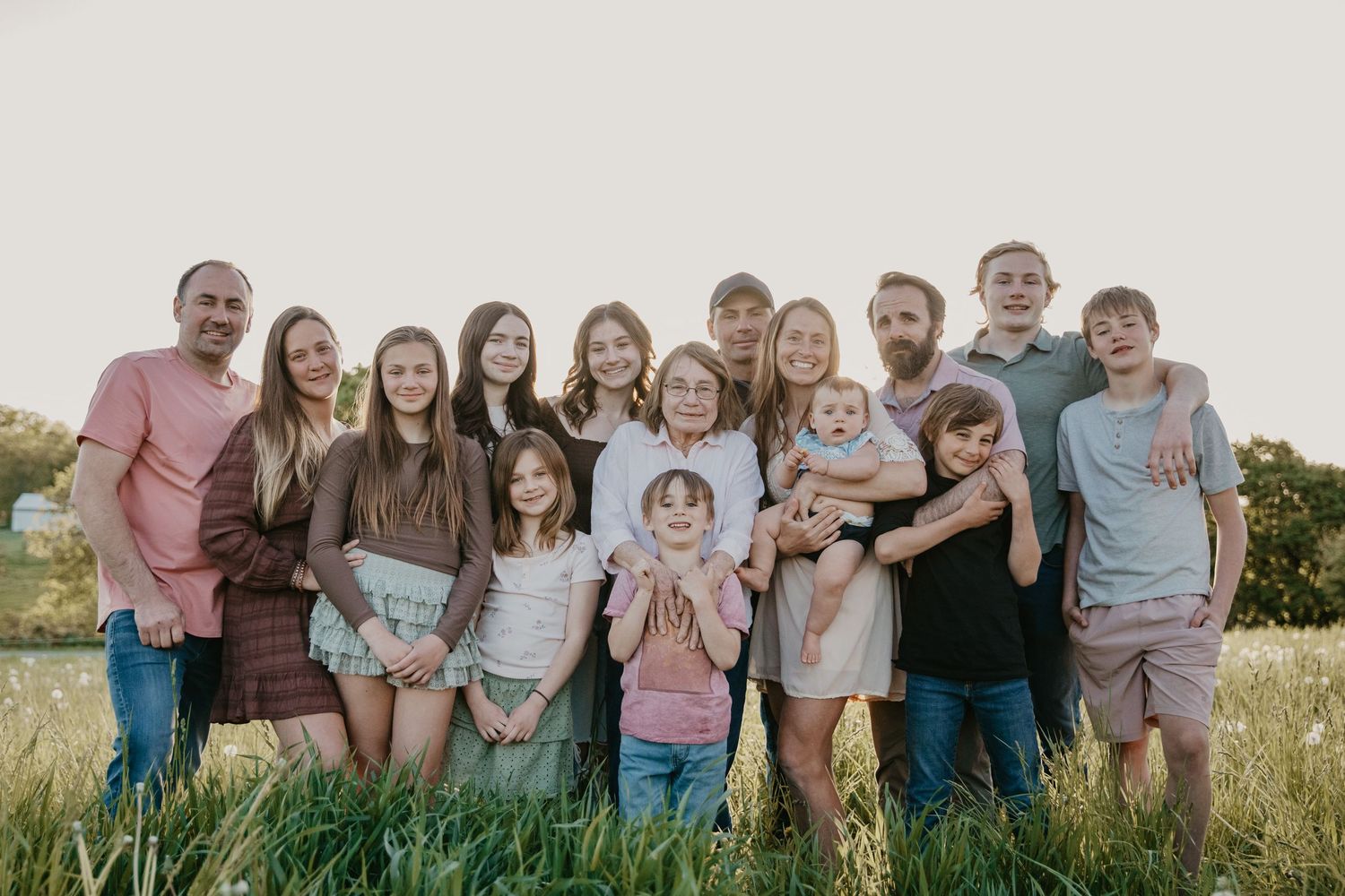 Large family group poses together outdoors in coordinated casual outfits.