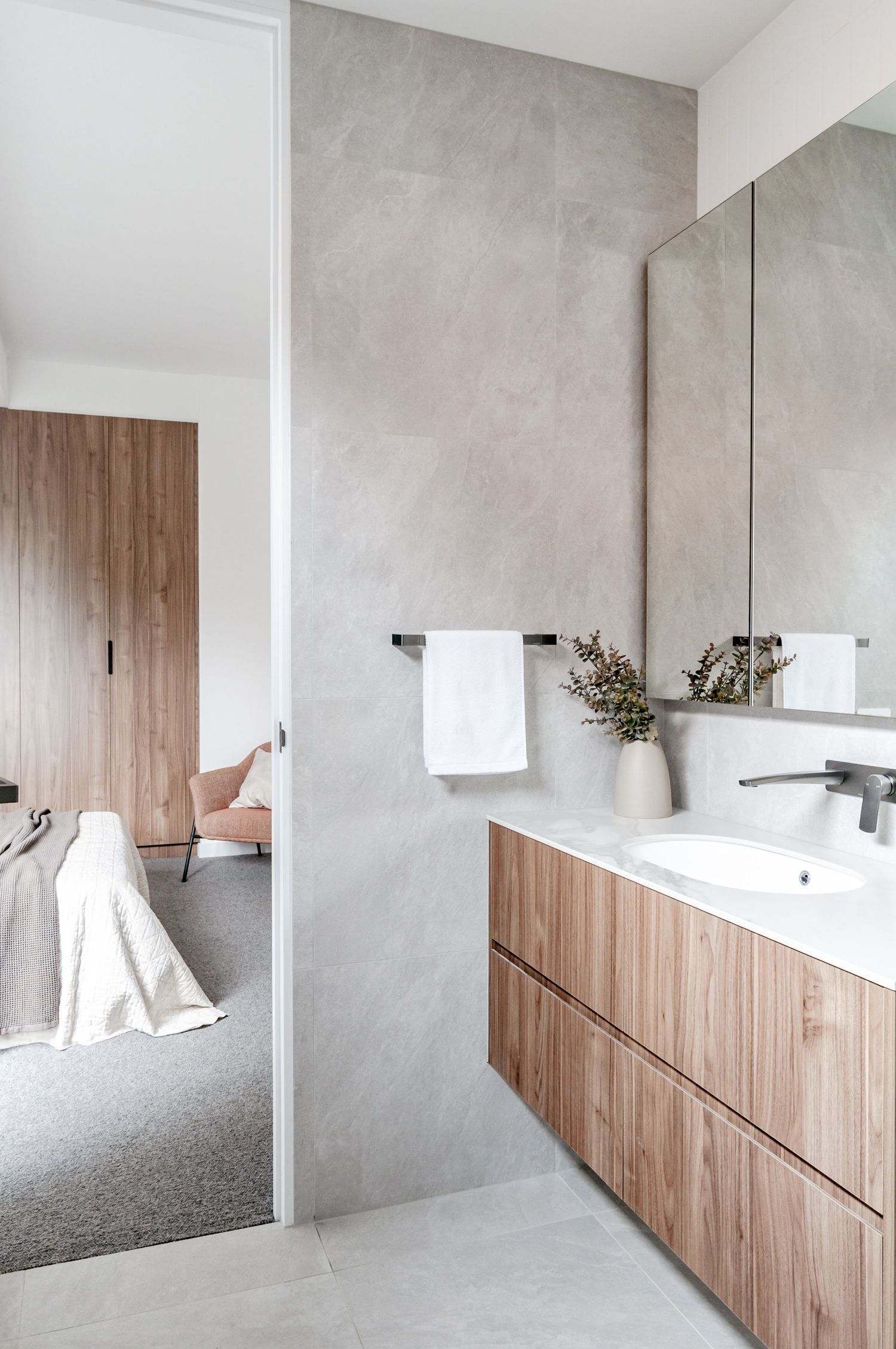 Sleek bathroom interior with wood cabinetry, concrete-look walls, and large mirror reflecting natural light.