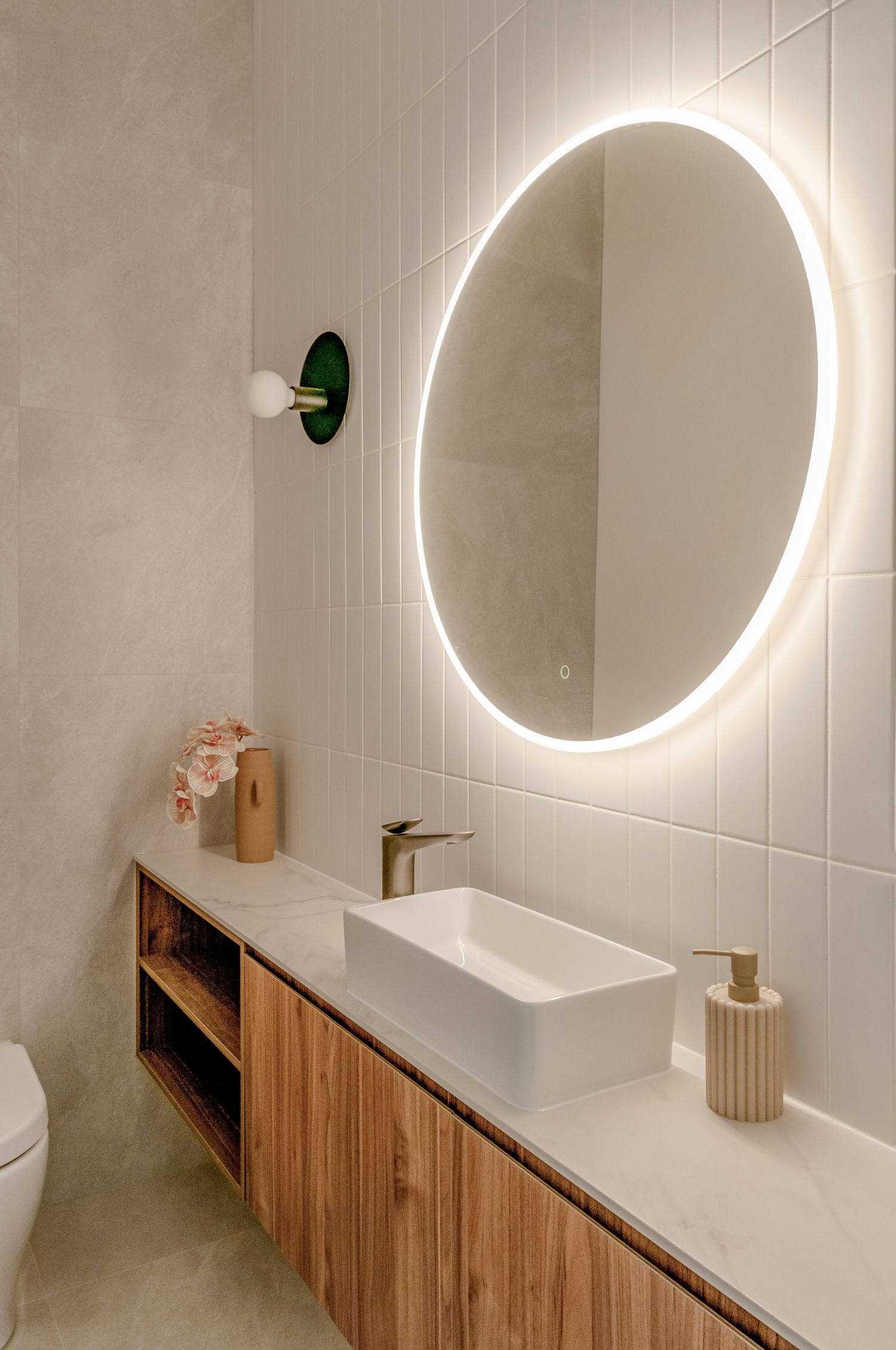 Modern bathroom vanity with circular LED mirror, white walls and wooden storage cabinet underneath.