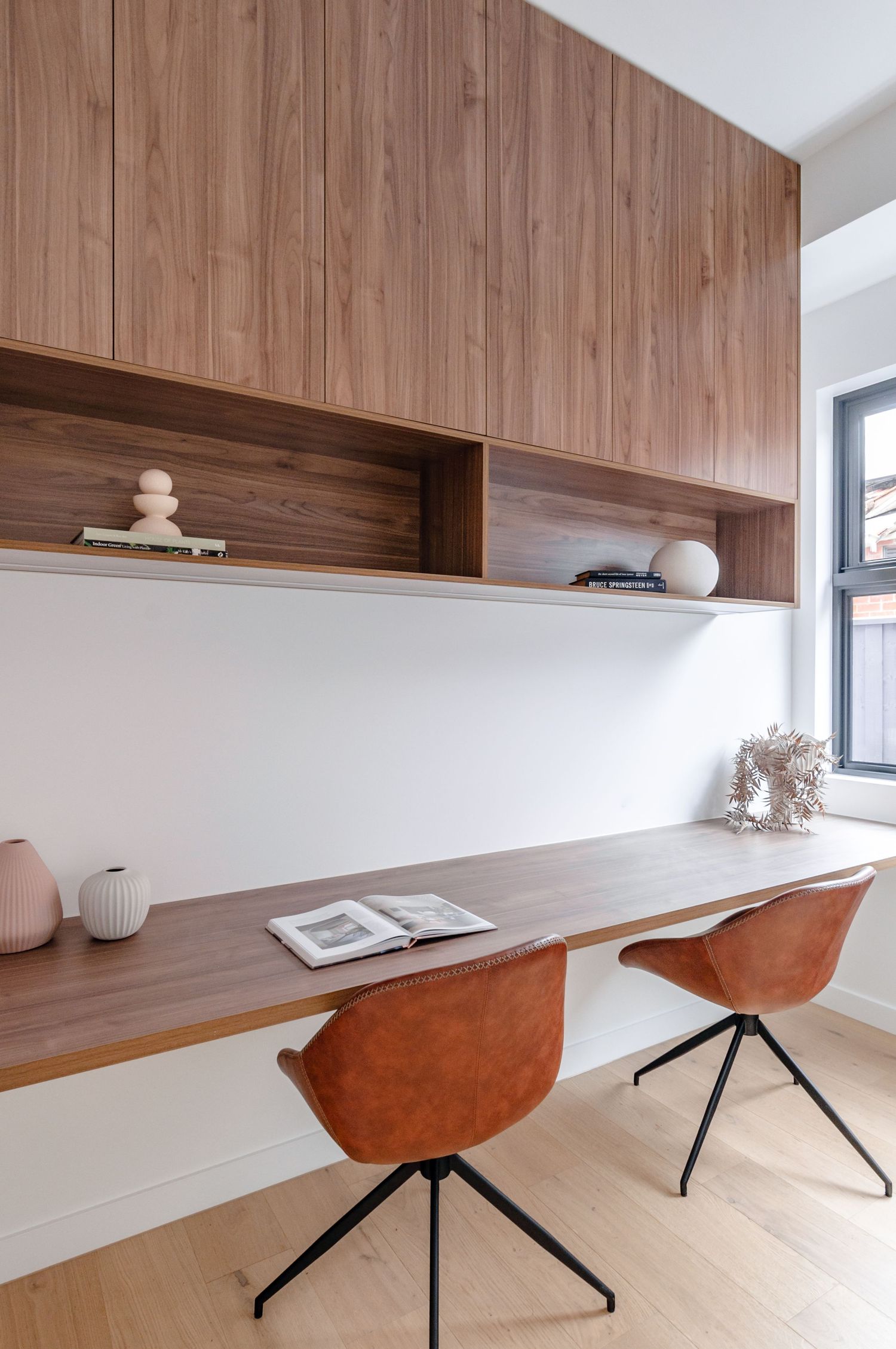 Modern home office space with floating wooden desk, brown leather chairs and built-in wood shelving.