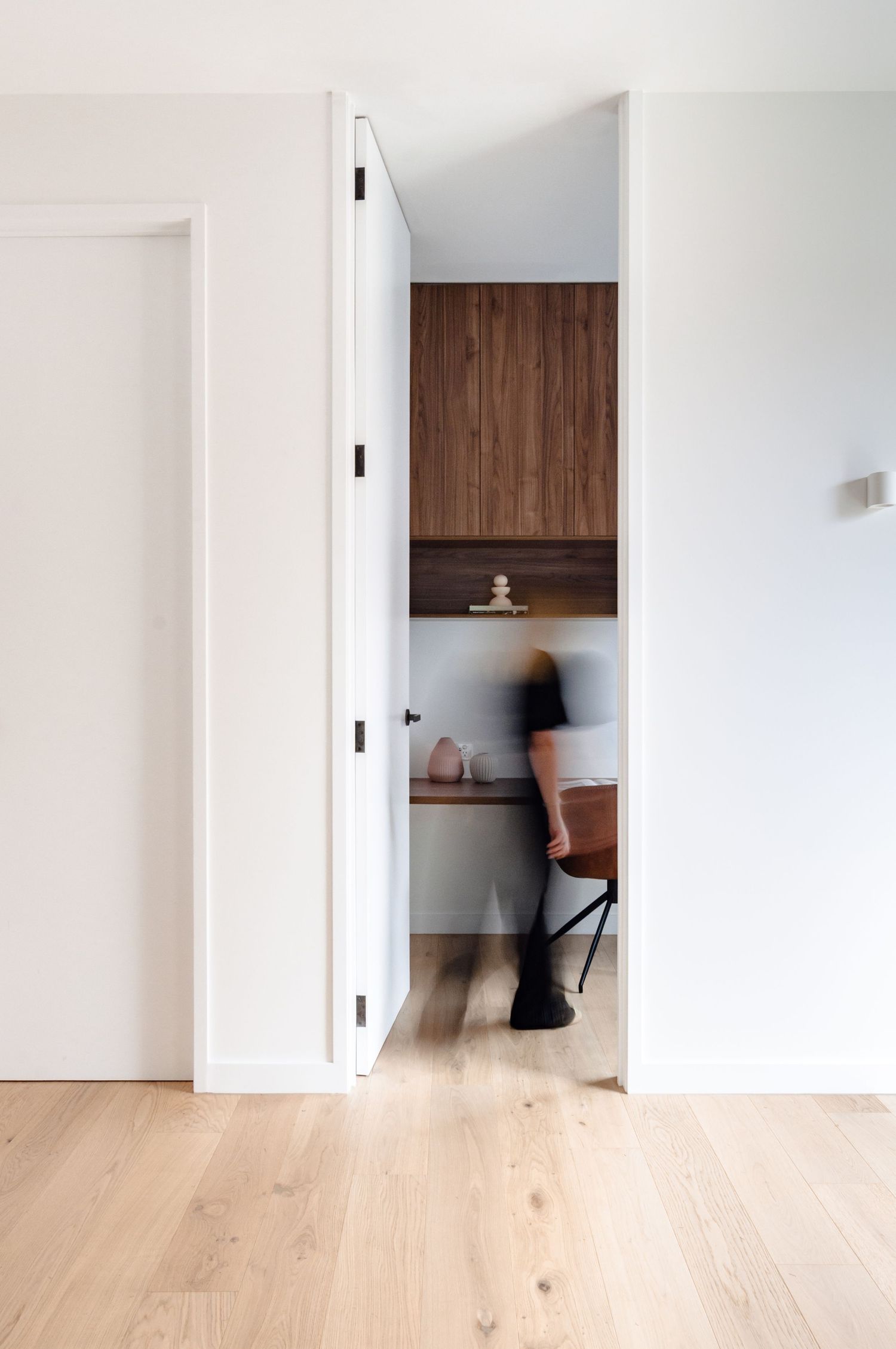 Contemporary hallway with white walls, light wood flooring, and doorways leading to rooms with warm wood accents.