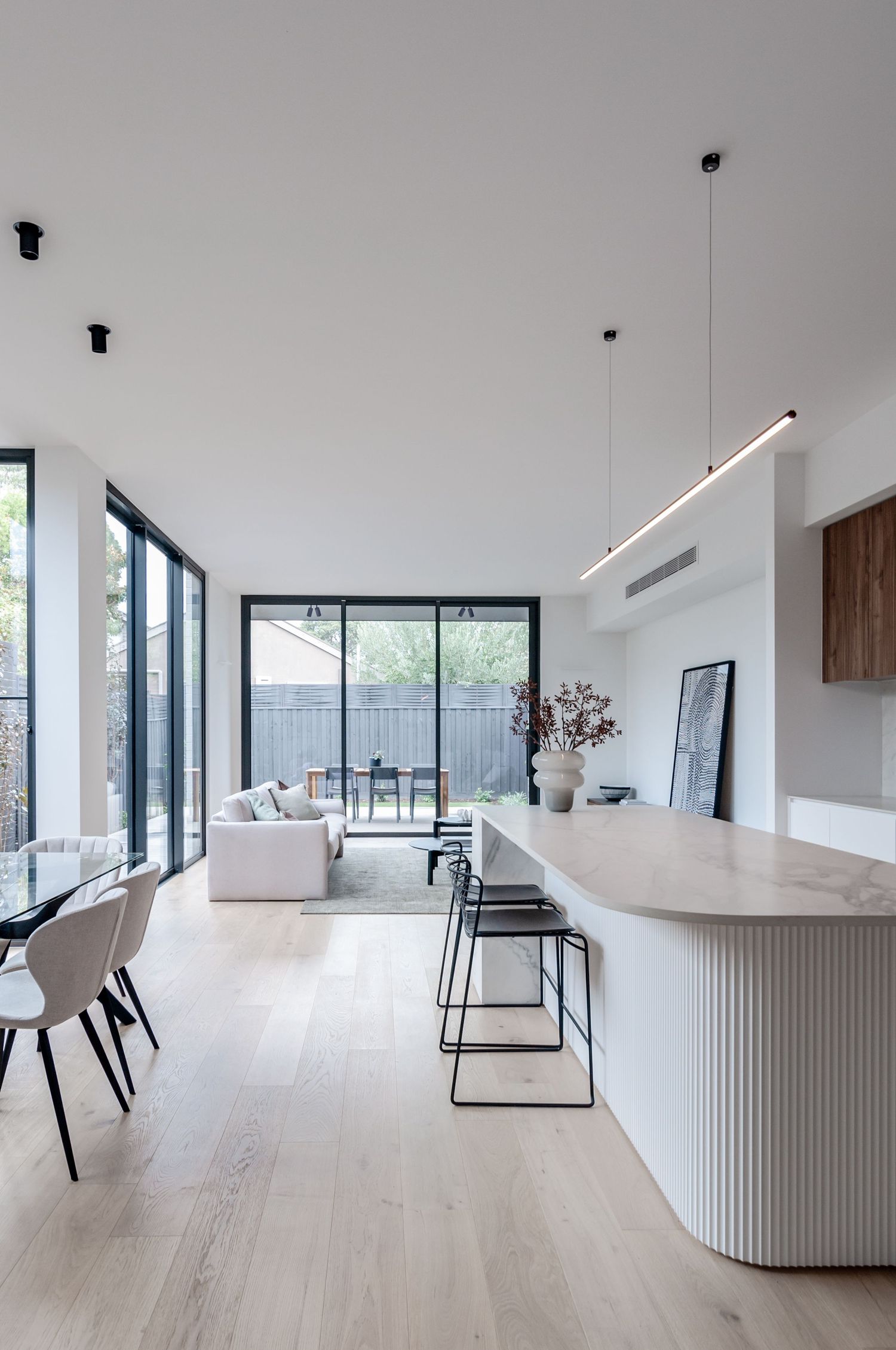 Contemporary white dining area featuring sleek furniture, light wood floors and floor-to-ceiling windows.