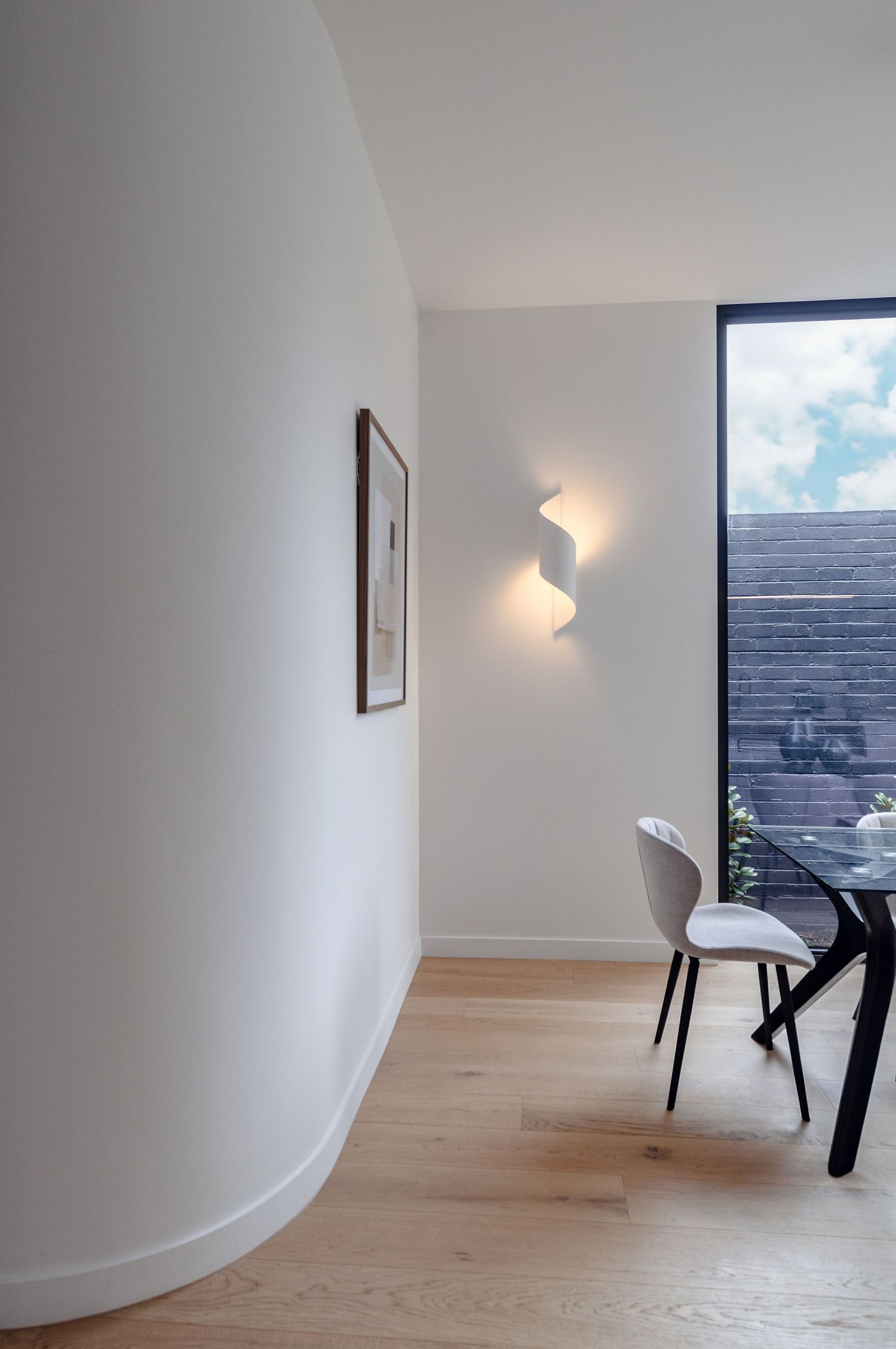 Contemporary curved wall interior with wooden flooring and modern wall sconce lighting.