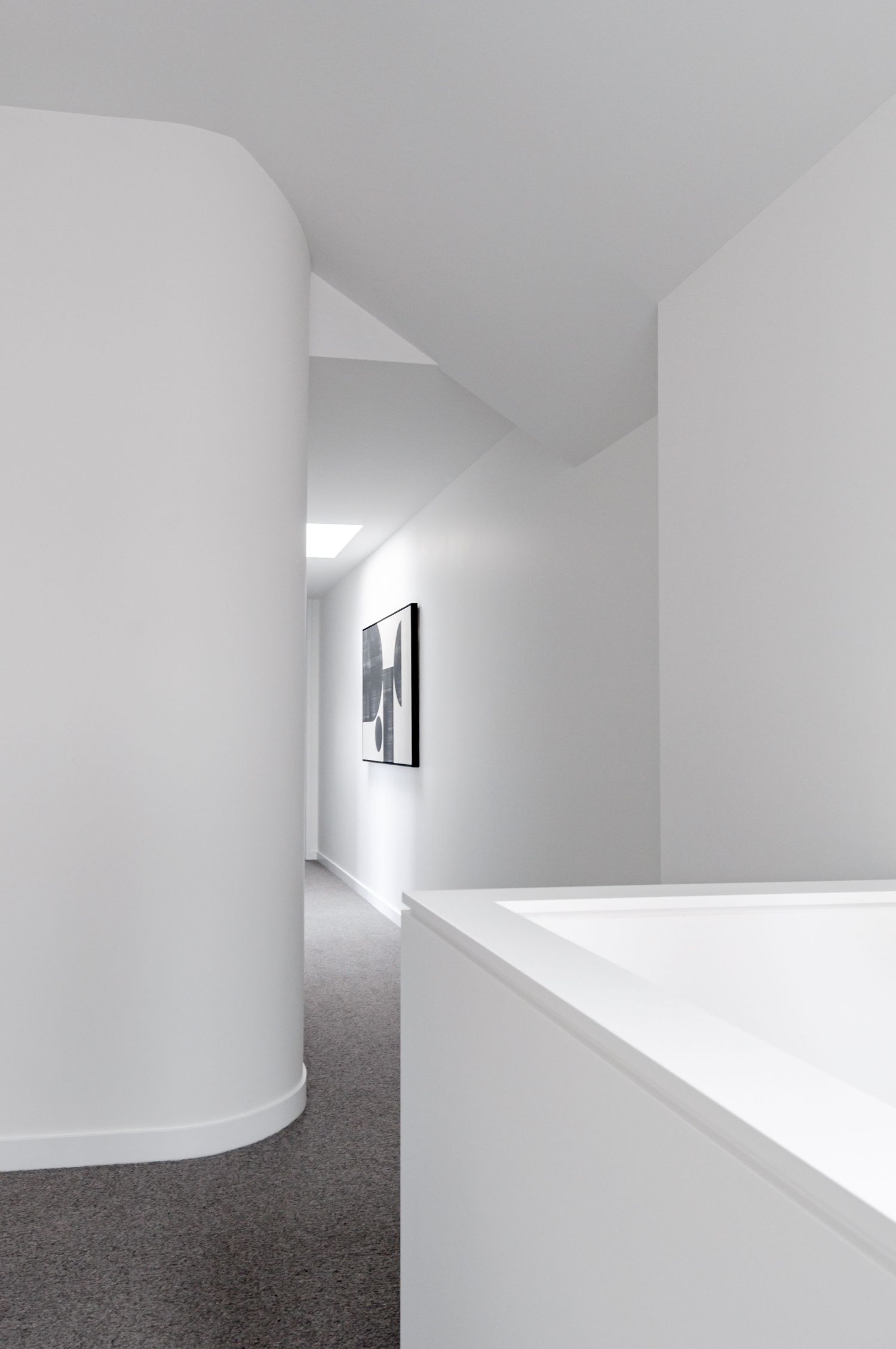 Sleek white interior hallway with curved walls and dramatic natural lighting from above.
