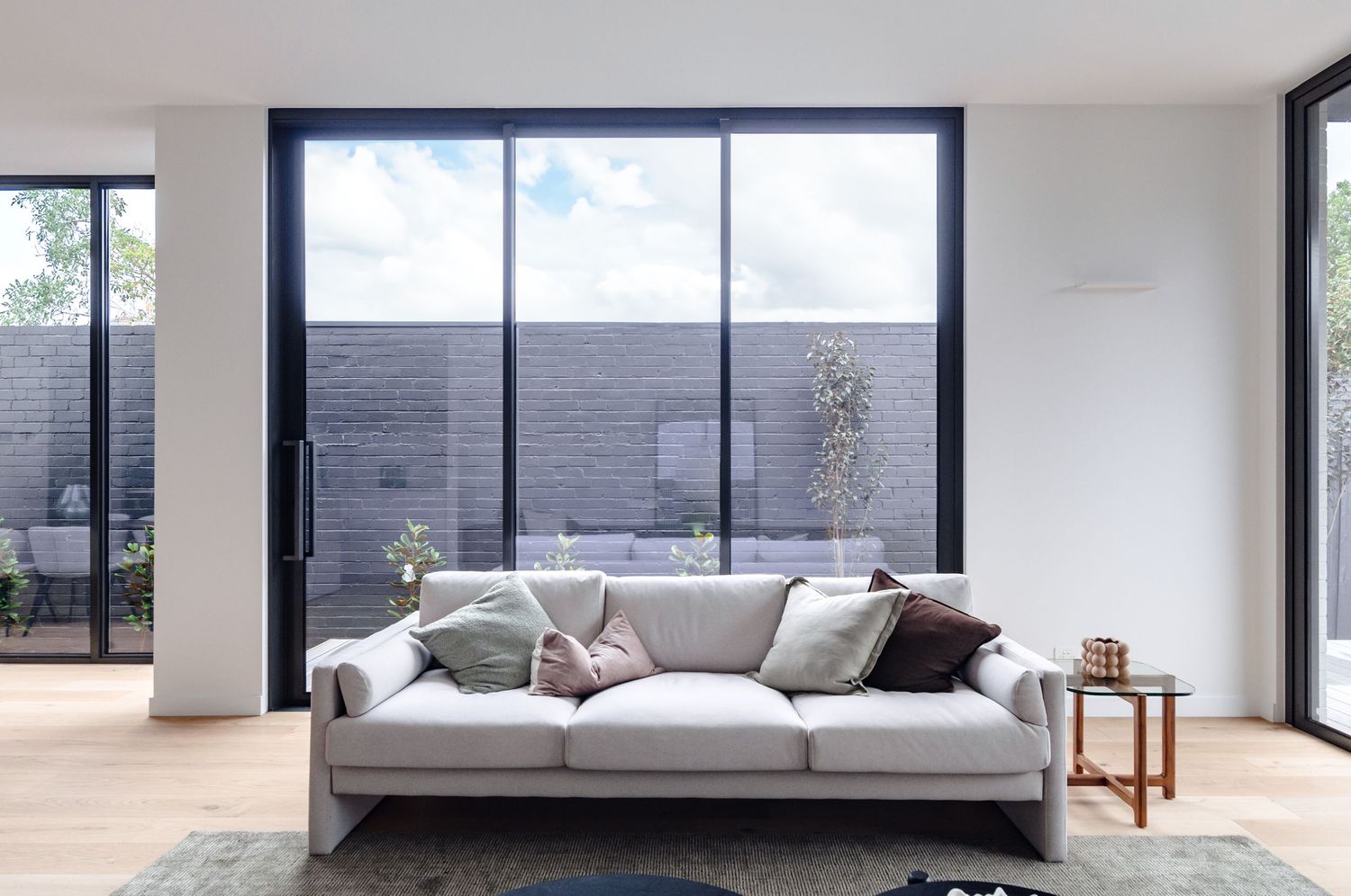 Spacious modern living room interior with large windows, grey sofa, and contemporary decor.
