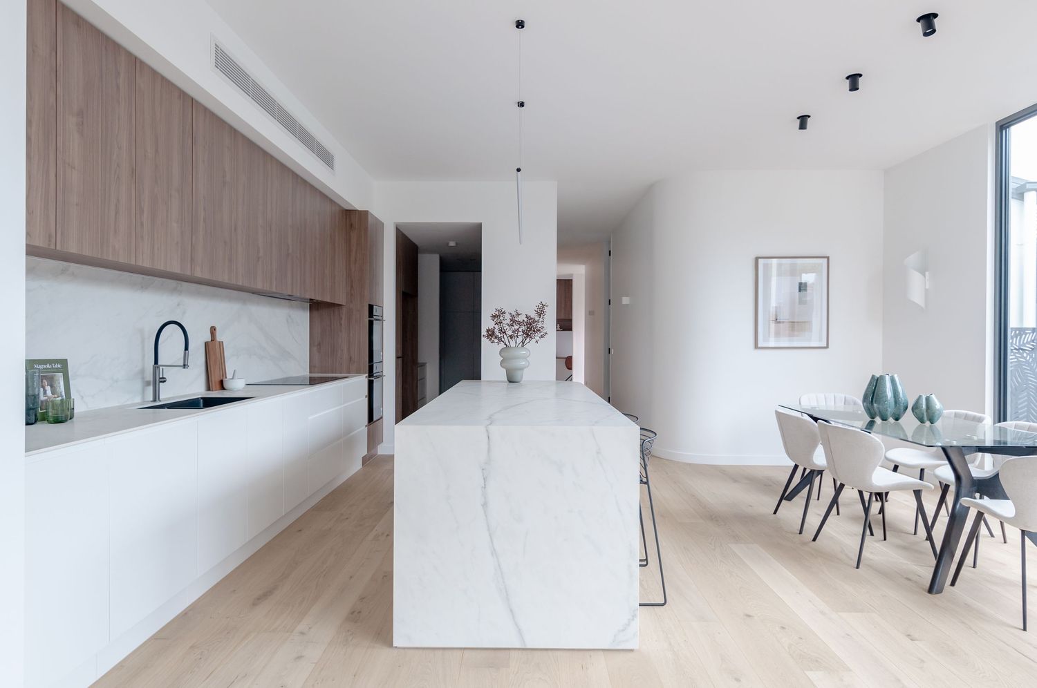 Modern open concept kitchen features white marble waterfall island, light wood cabinets and hardwood floors in bright airy space.