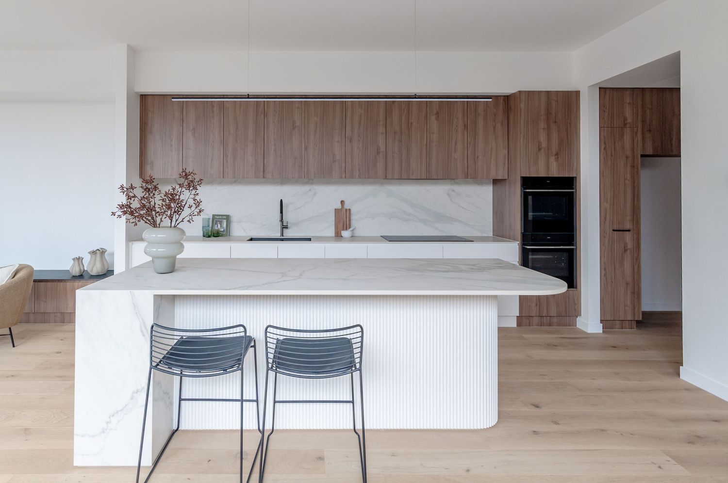 Minimalist kitchen with white countertops, wood cabinetry and modern pendant lighting against clean white walls.