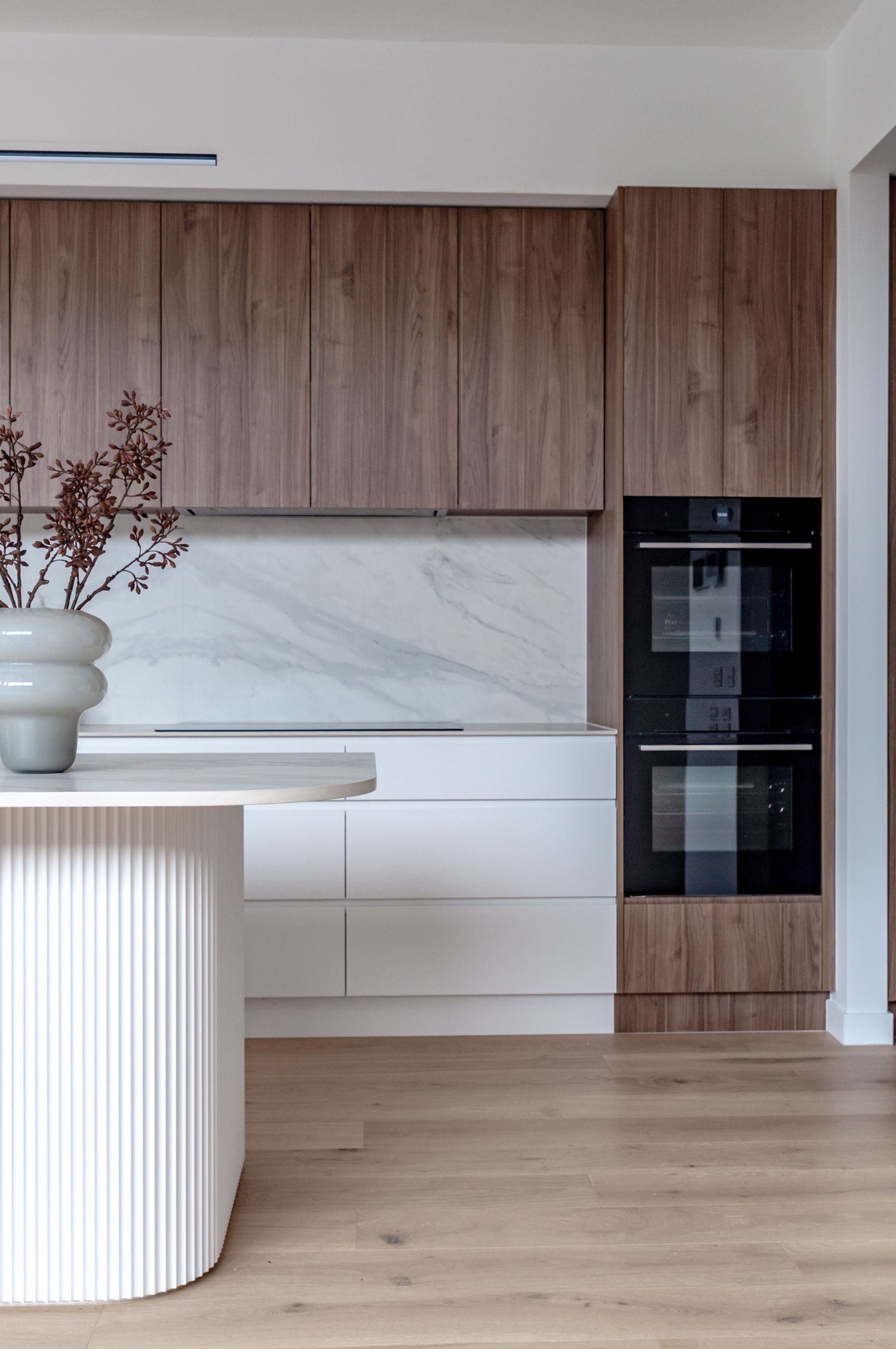 Contemporary kitchen design featuring white and wood cabinetry with fluted island and marble countertops.