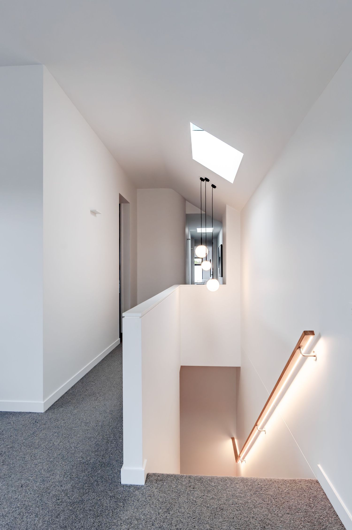 Minimalist white hallway with grey carpet and angled skylights casting dramatic shadows across the walls.