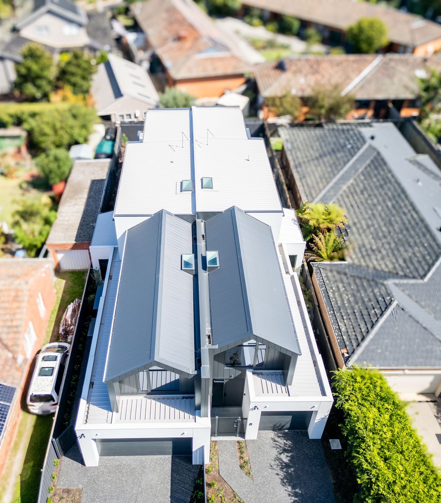 Aerial view of modern white house with grey roof panels and surrounding suburban neighborhood.