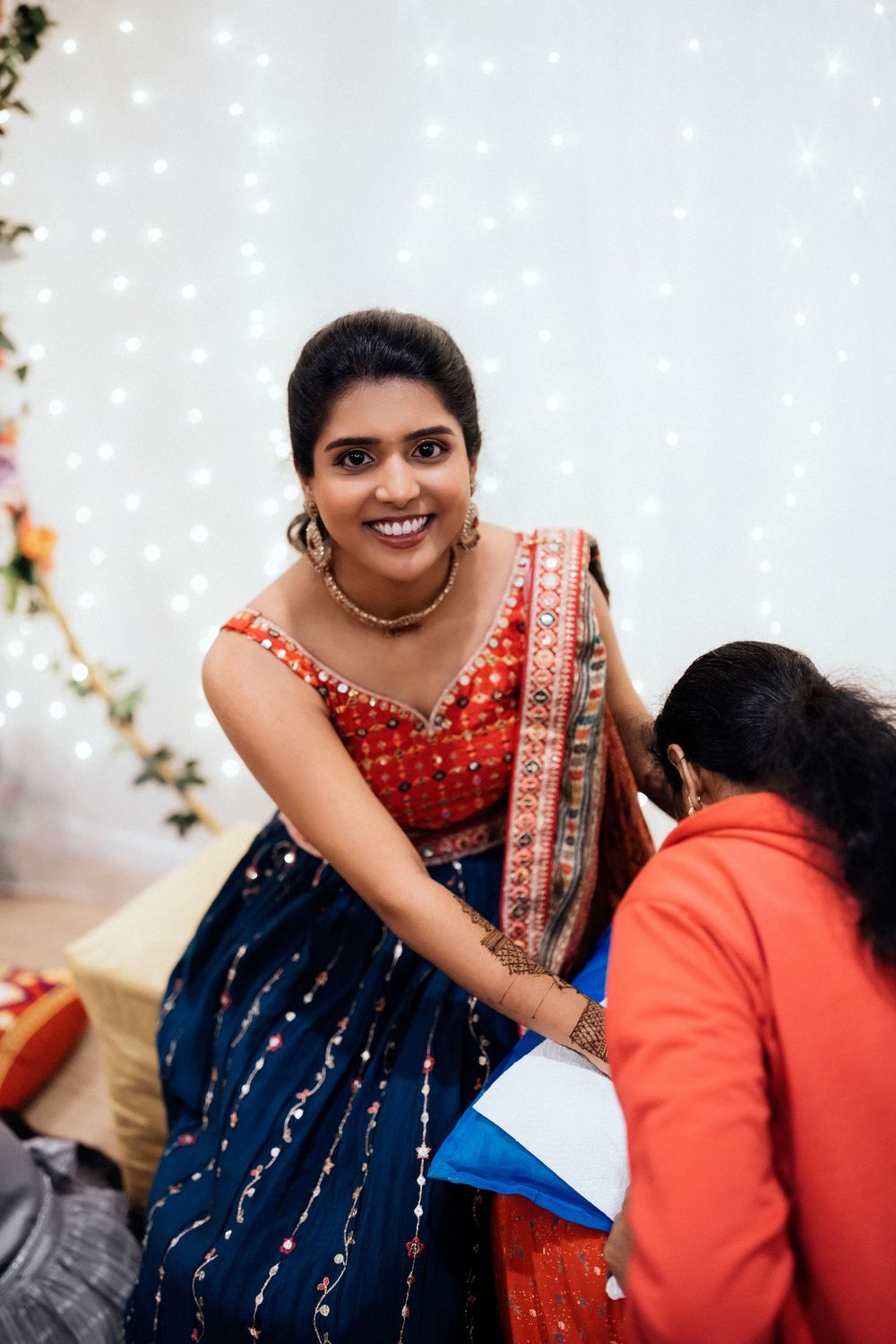 A woman in a red and navy blue traditional Indian sari dress smiles during what appears to be a festive celebration.