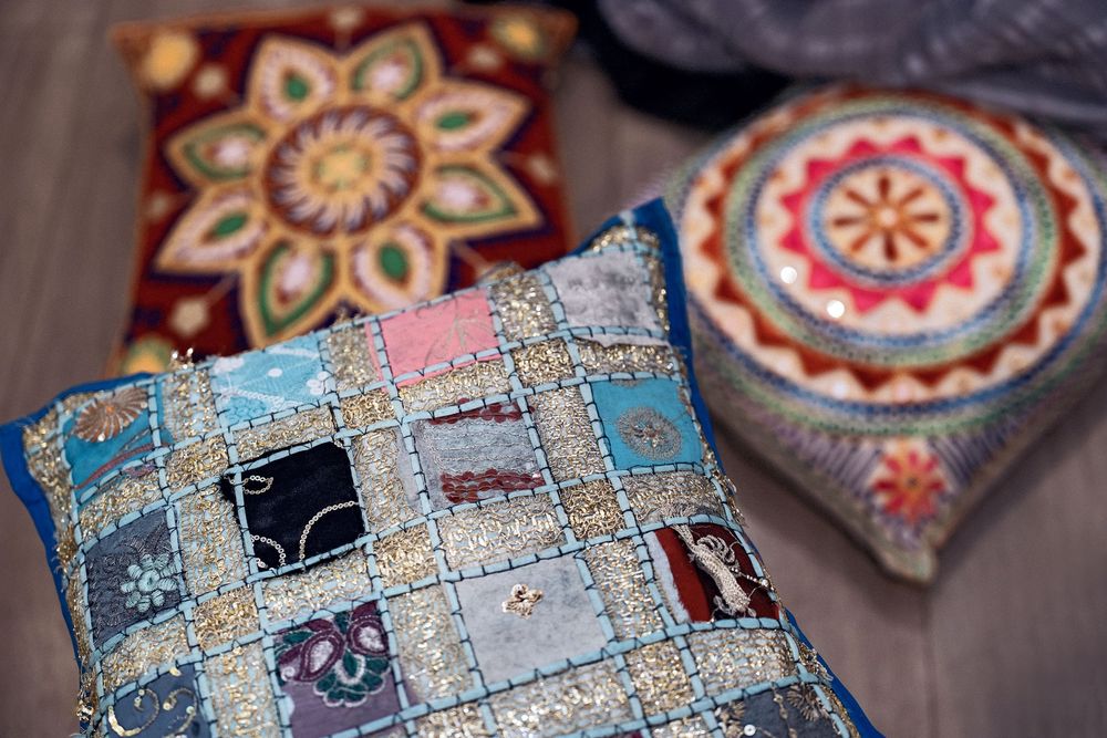 Decorative throw pillows with intricate patchwork and embroidered patterns in blue, pink, and earthy tones on a wooden surface.