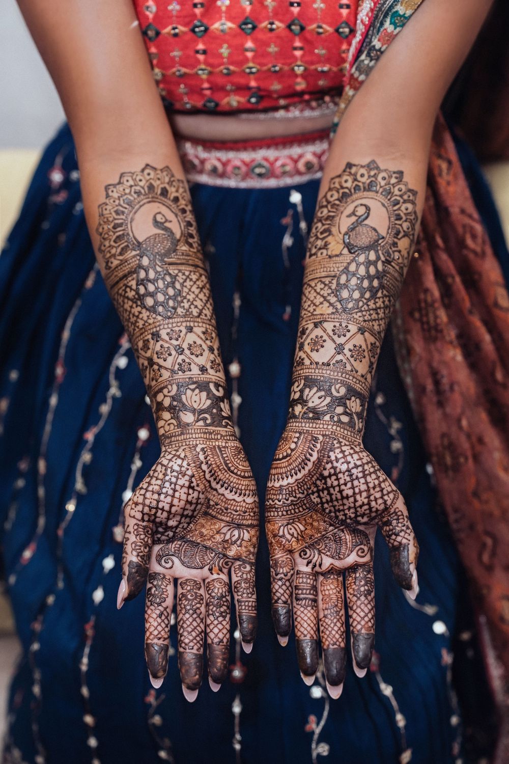 Beautiful bridal mehndi designs showing intricate floral and geometric patterns on both hands against dark fabric background.